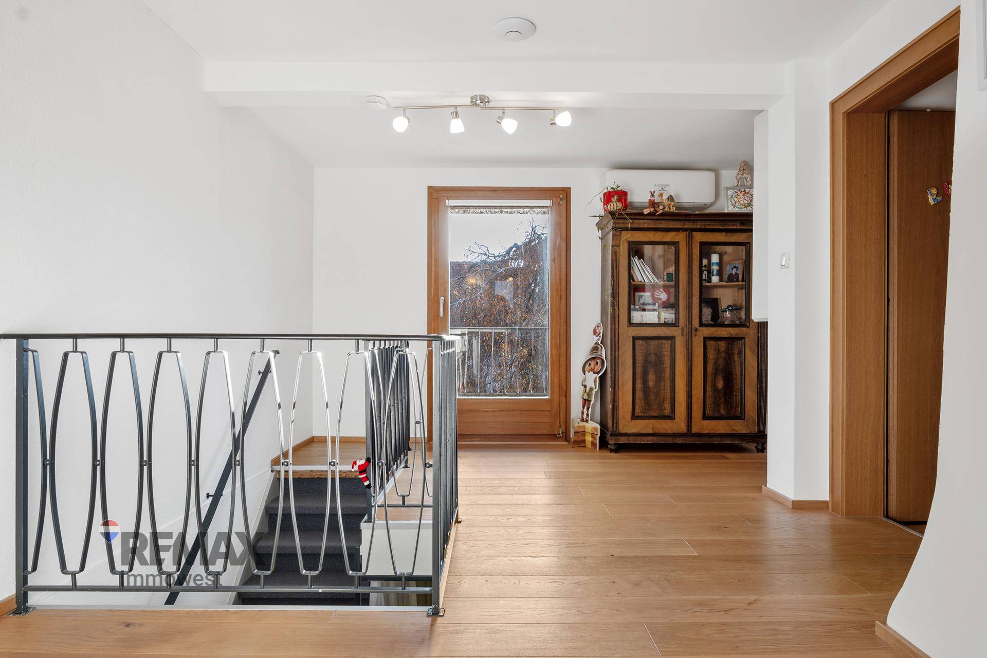 Heller Flur im Obergeschoss mit Holzfußboden, Treppe und Zugang zu einem Außenbereich.
