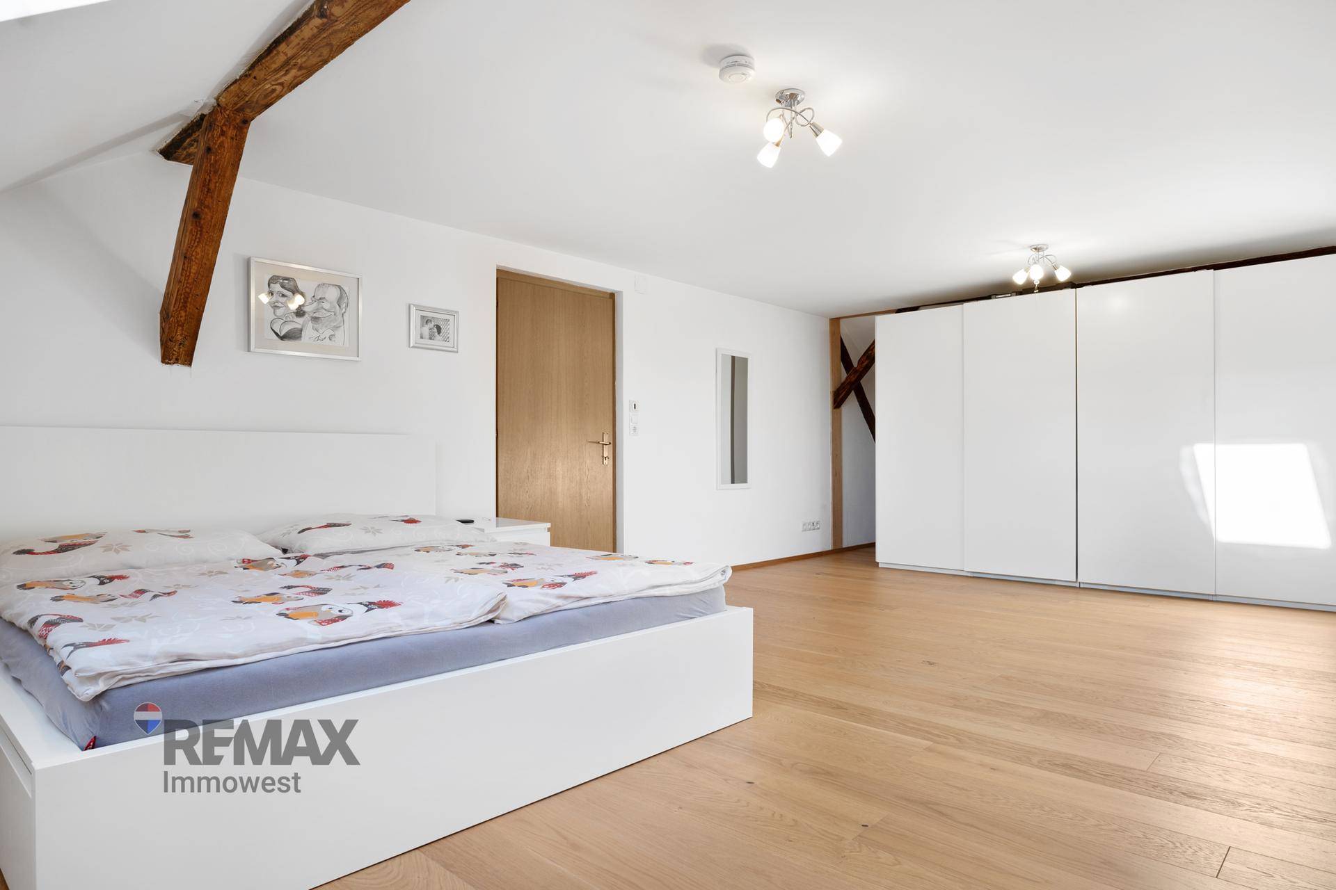 Helles Schlafzimmer mit weißem Bett, Kleiderschränken und Holzboden, sichtbarer Holzbalken.