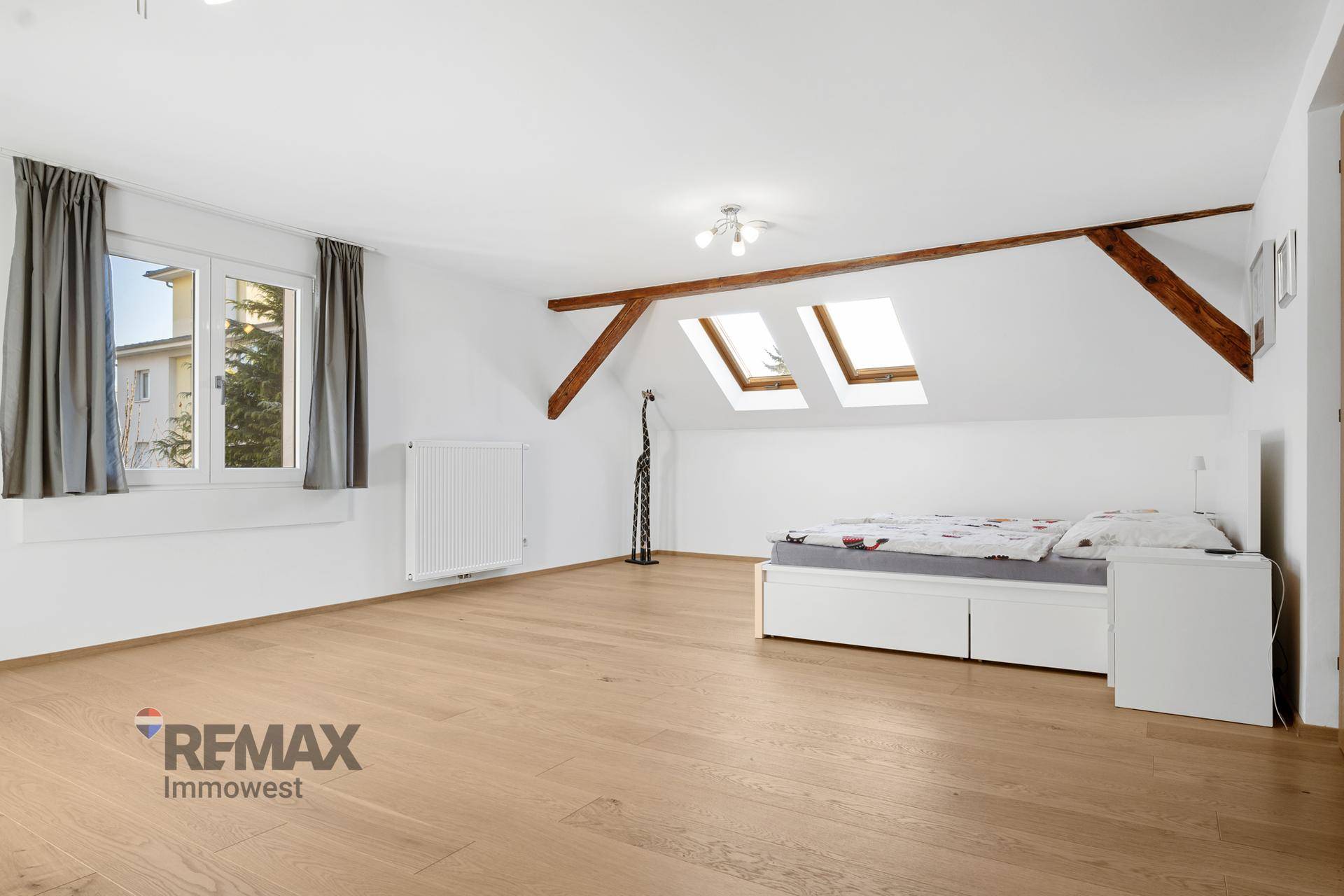 Geräumiges Schlafzimmer mit Bett, großem Fenster, zwei Dachfenstern und Holzboden.