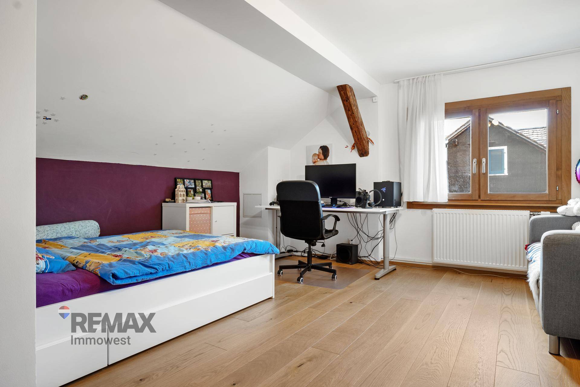 Schlafzimmer mit Arbeitsbereich, Bett, violetter Akzentwand und Holzboden.