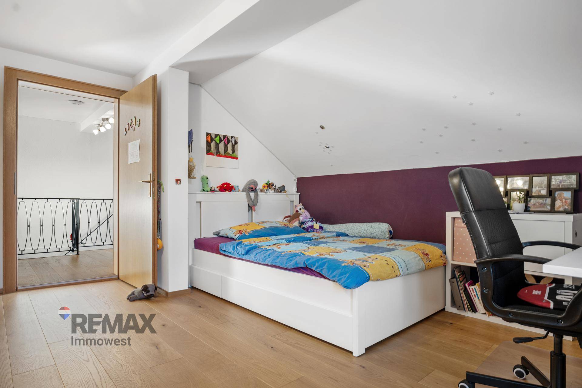 Ansicht des Schlafzimmers mit Bett, Schreibtisch und Zugang zum Flur, unter Dachschräge.