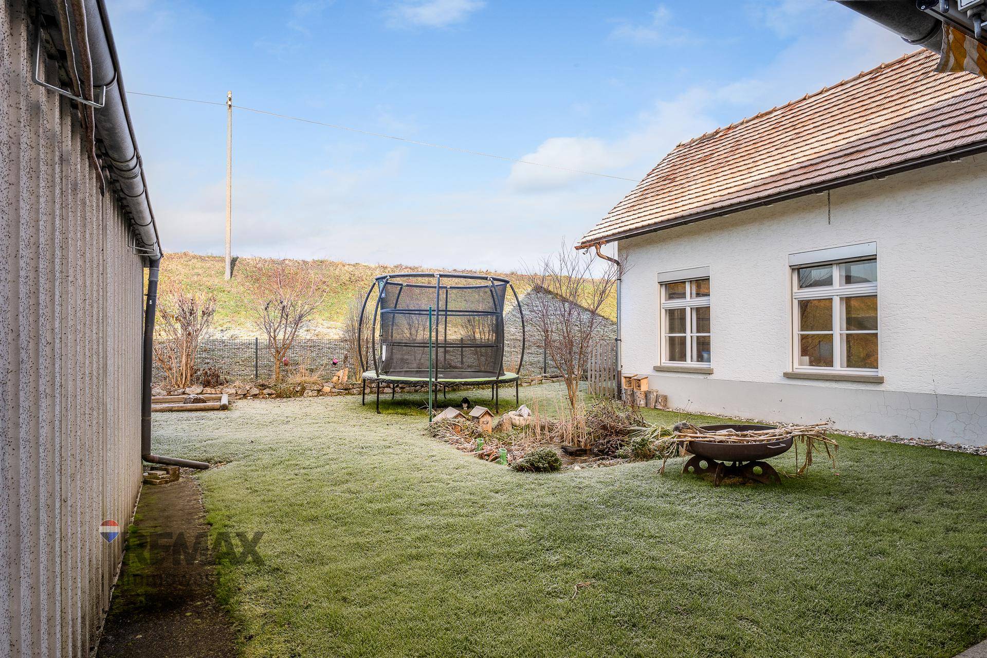 Hinterhof mit Rasenfläche, Trampolin und Feuerstelle, neben dem Haus.