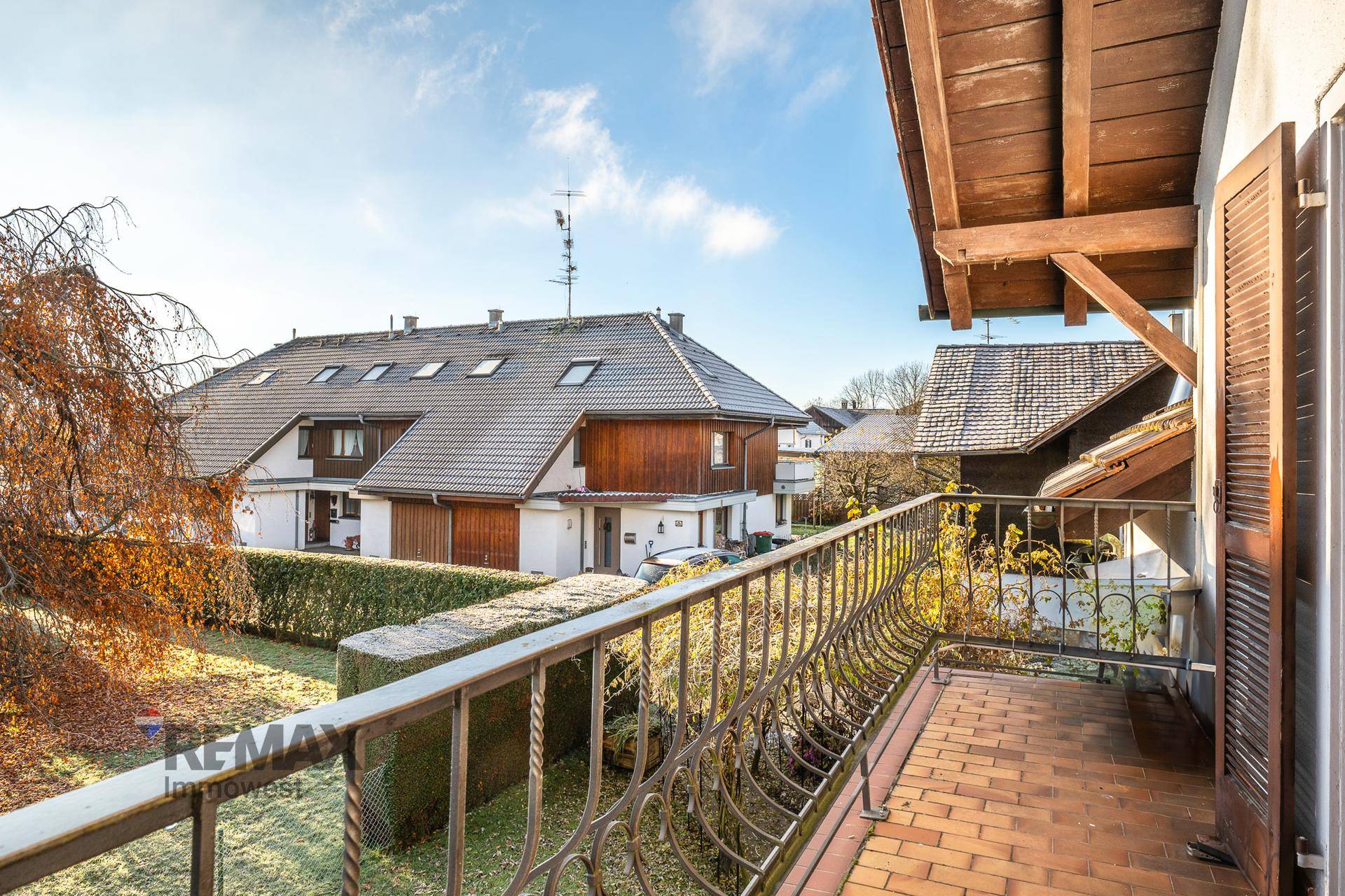Balkon mit schmiedeeisernem Geländer und Fliesenboden, Blick auf Nachbarhäuser und Garten.