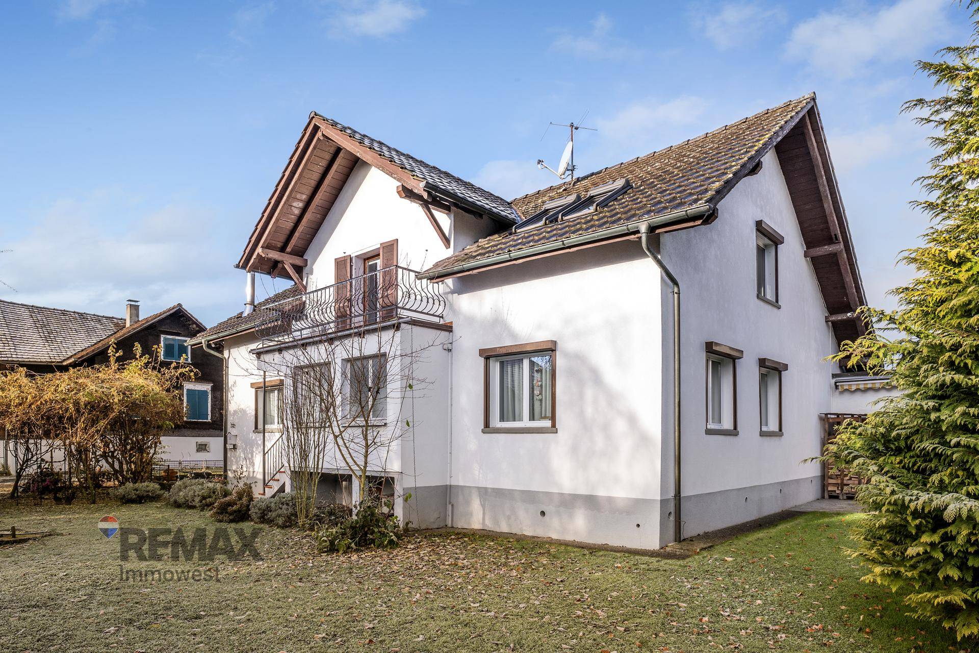 Seitenansicht des Hauses mit kleinem Rasenbereich und einem Balkon im Obergeschoss.