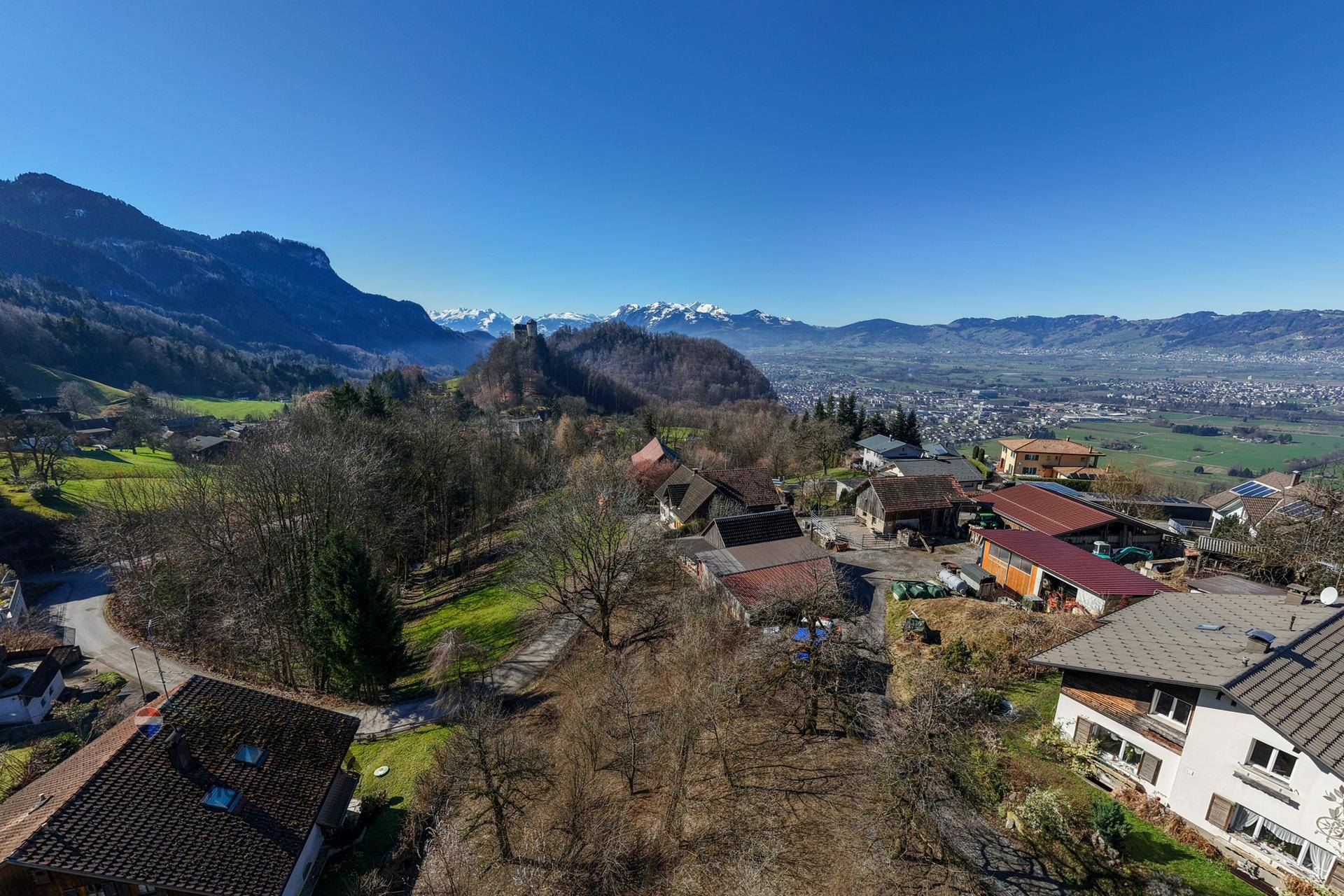 Panoramablick über eine ländliche Siedlung mit weitem Horizont und schneebedeckten Bergen in der Ferne.