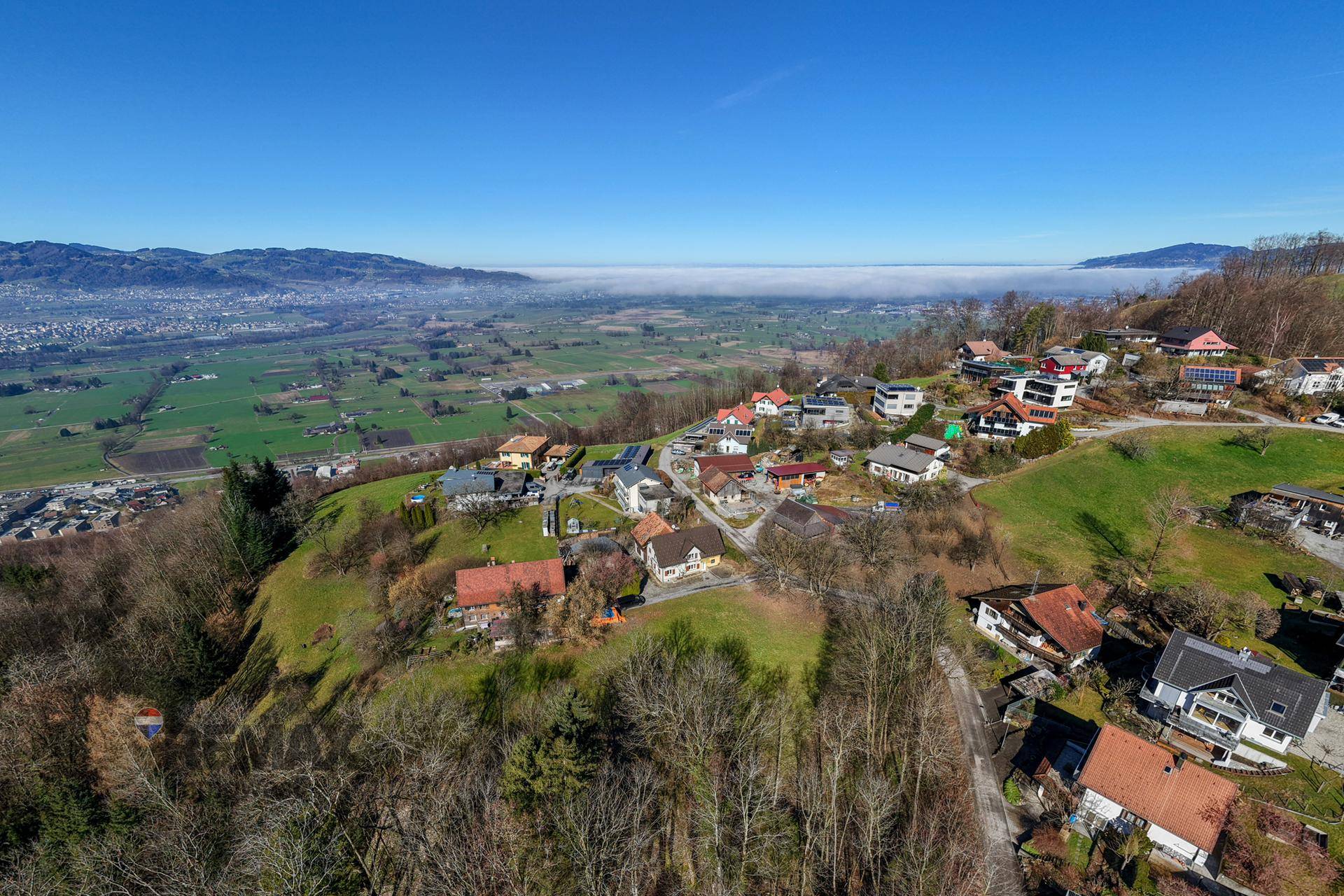 Weitläufige Luftaufnahme einer Siedlung in hügeliger Landschaft mit weitem Blick über das Tal und die Berge.