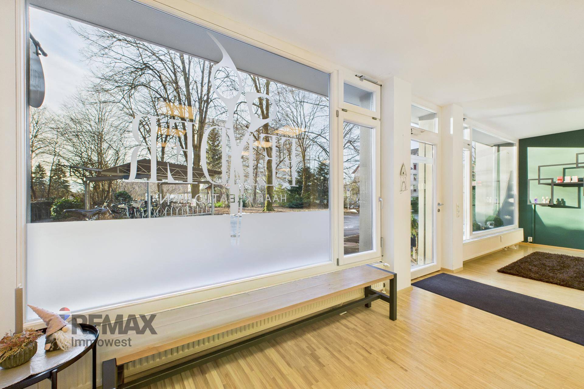 Eingangsbereich eines Salons mit großen Fenstern, einer Sitzbank und Blick auf die winterliche Umgebung.