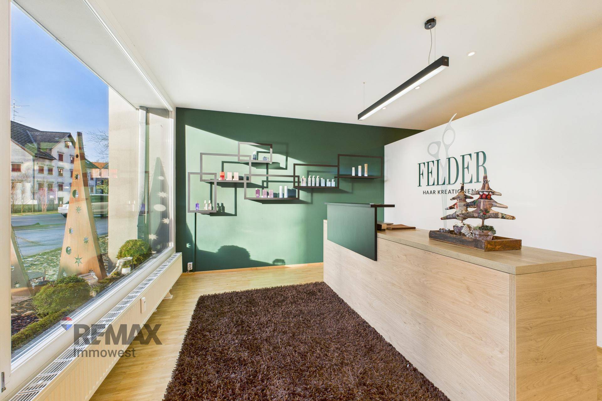 Empfangsbereich eines modernen Salons mit Holztresen, grüner Akzentwand und großen Fenstern.