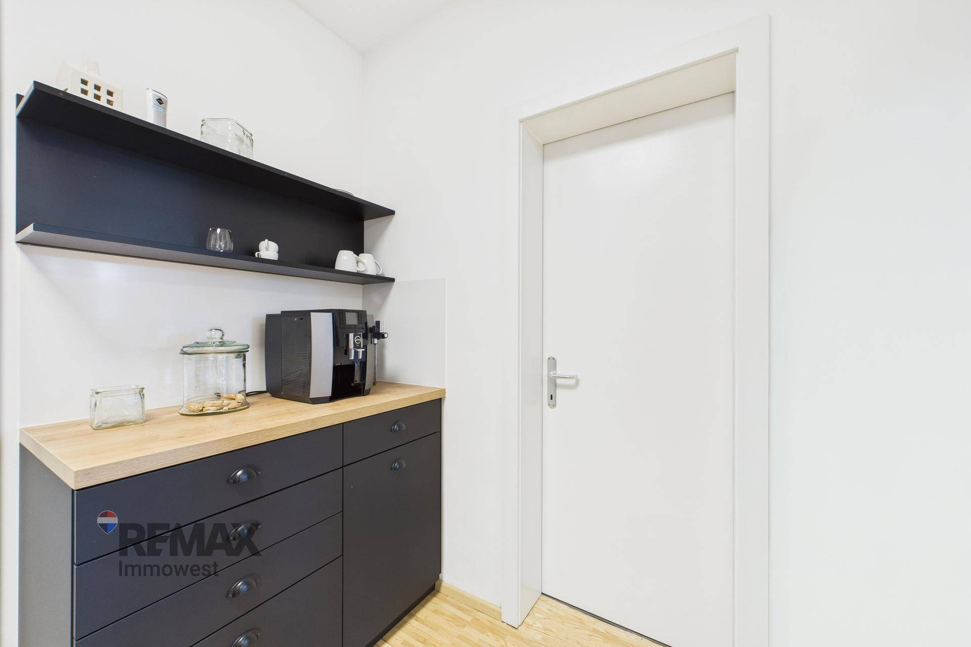 Kleiner Küchenbereich mit Kaffeemaschine, dunklen Schränken und Holztheke neben einer Tür.