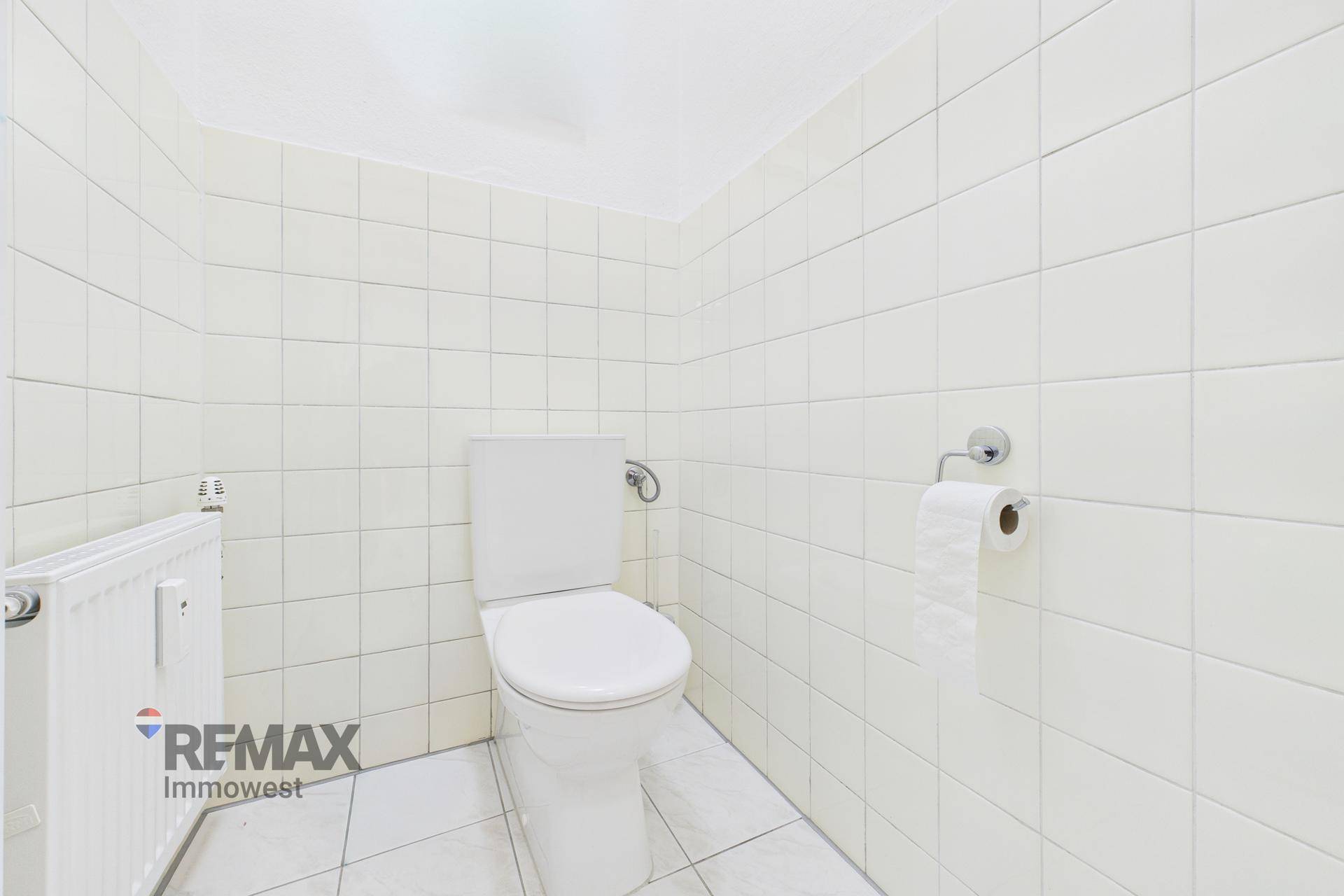 Separate Toilette mit weißer Keramik und hellen Fliesen an Wänden und Boden.