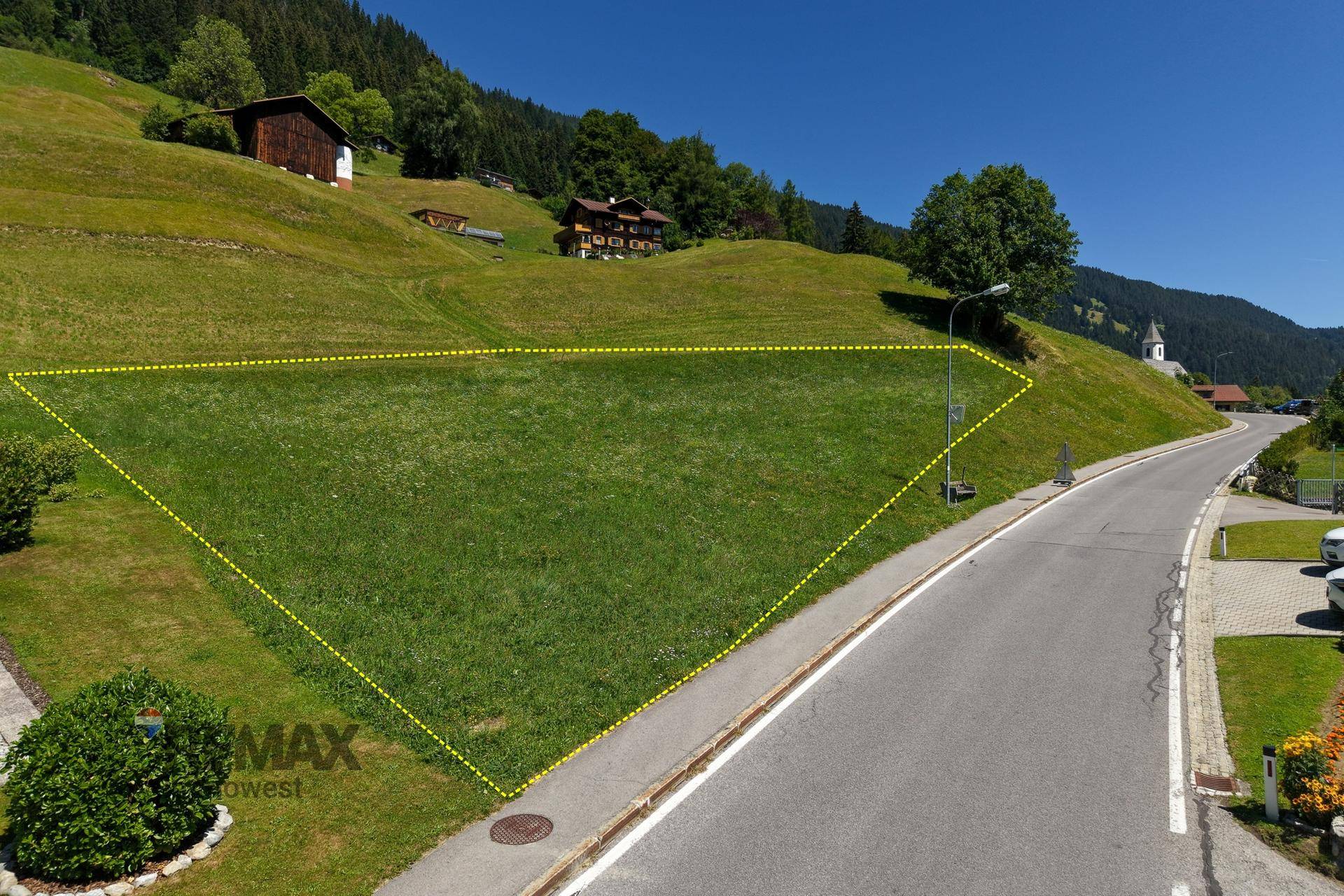 Grundstück an einer Straße in einer bergigen Landschaft mit umliegenden Häusern.