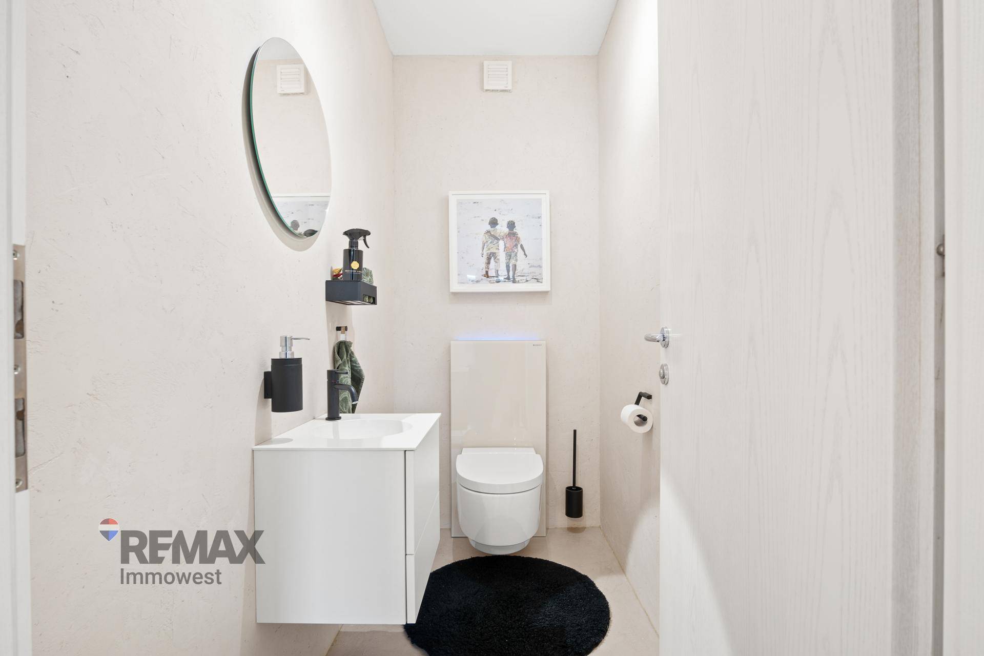 Modernes Gäste-WC mit wandhängendem WC, kleinem Waschbecken und ovalem Spiegel.