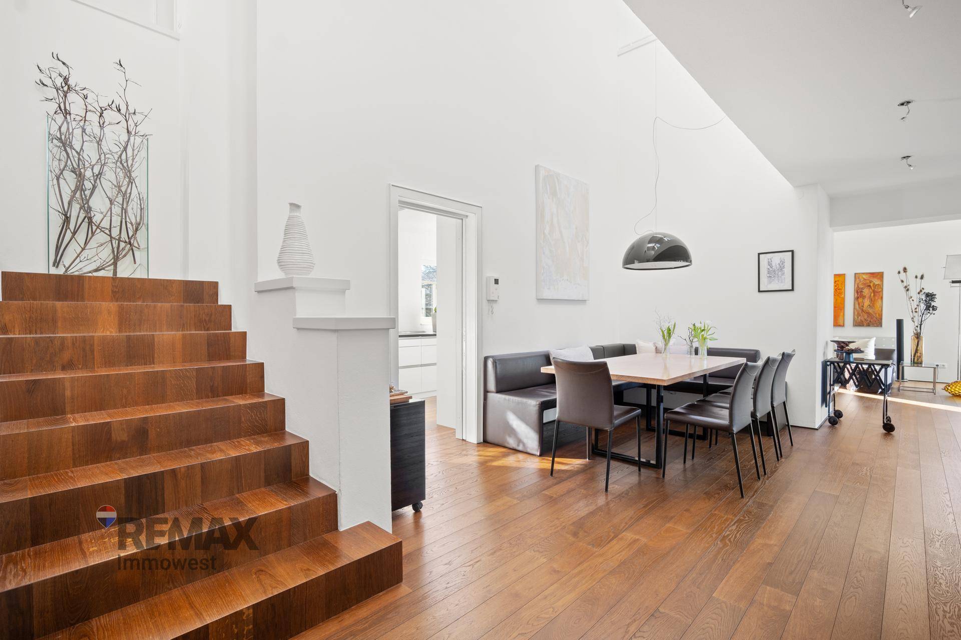 Offener Wohn- und Essbereich mit Holztreppe, Holzboden und modernem Esstisch.