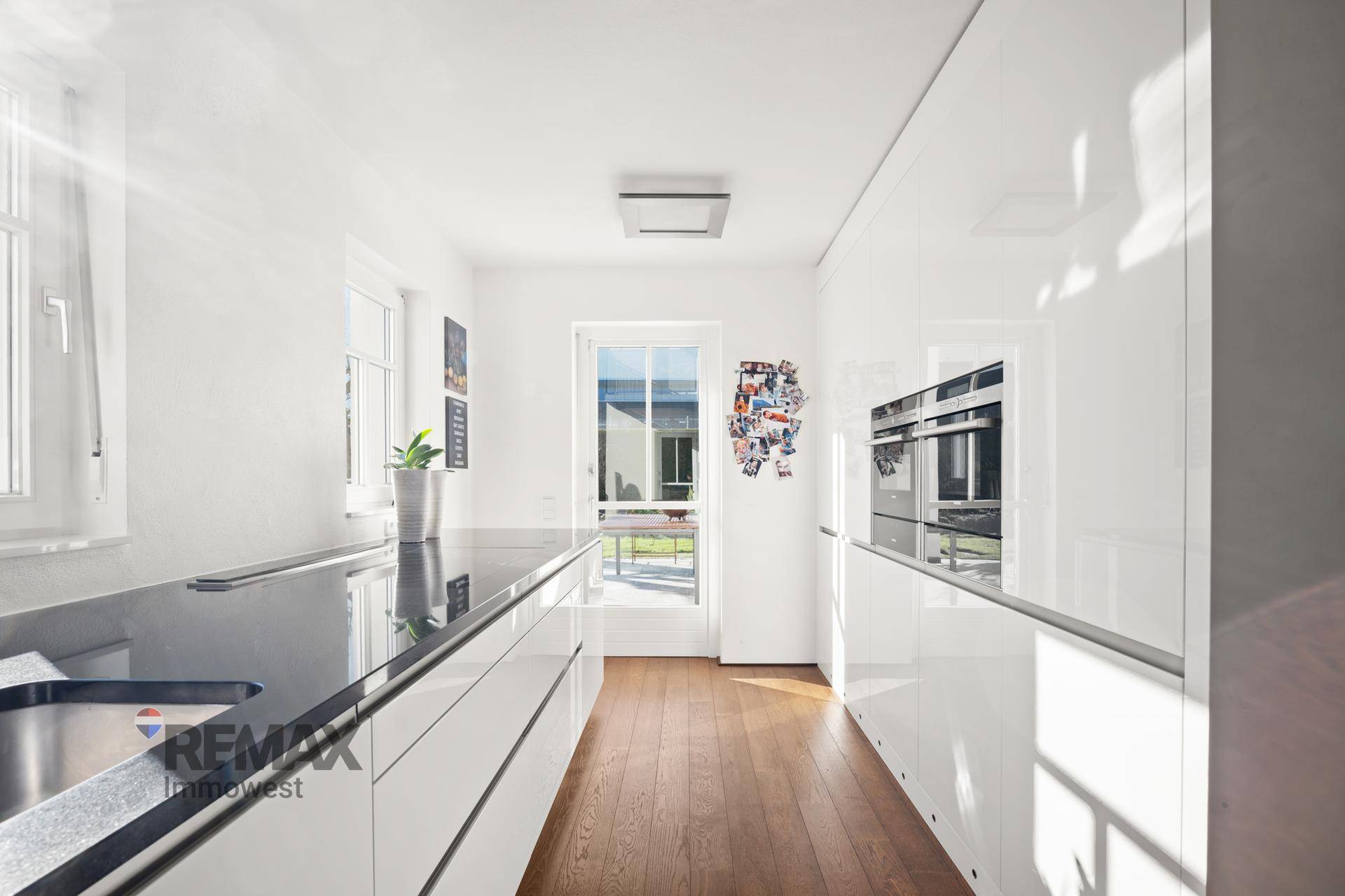 Moderne Küche mit weißen Hochglanzfronten, dunkler Arbeitsplatte und Holzboden.