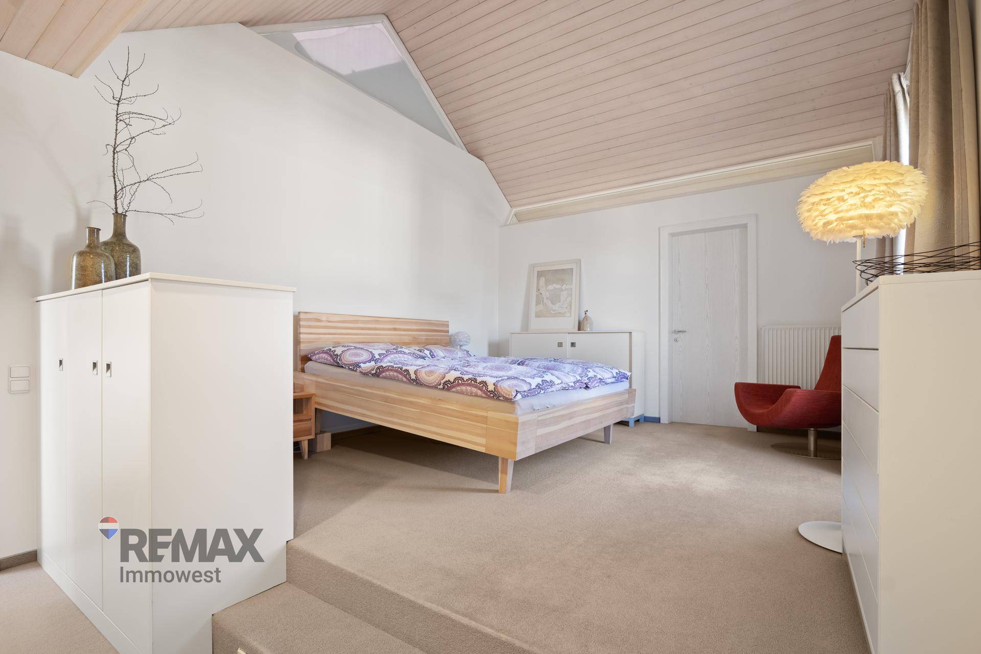 Gemütliches Schlafzimmer im Dachgeschoss mit Holzbett, Teppichboden und Holzdeckenverkleidung.
