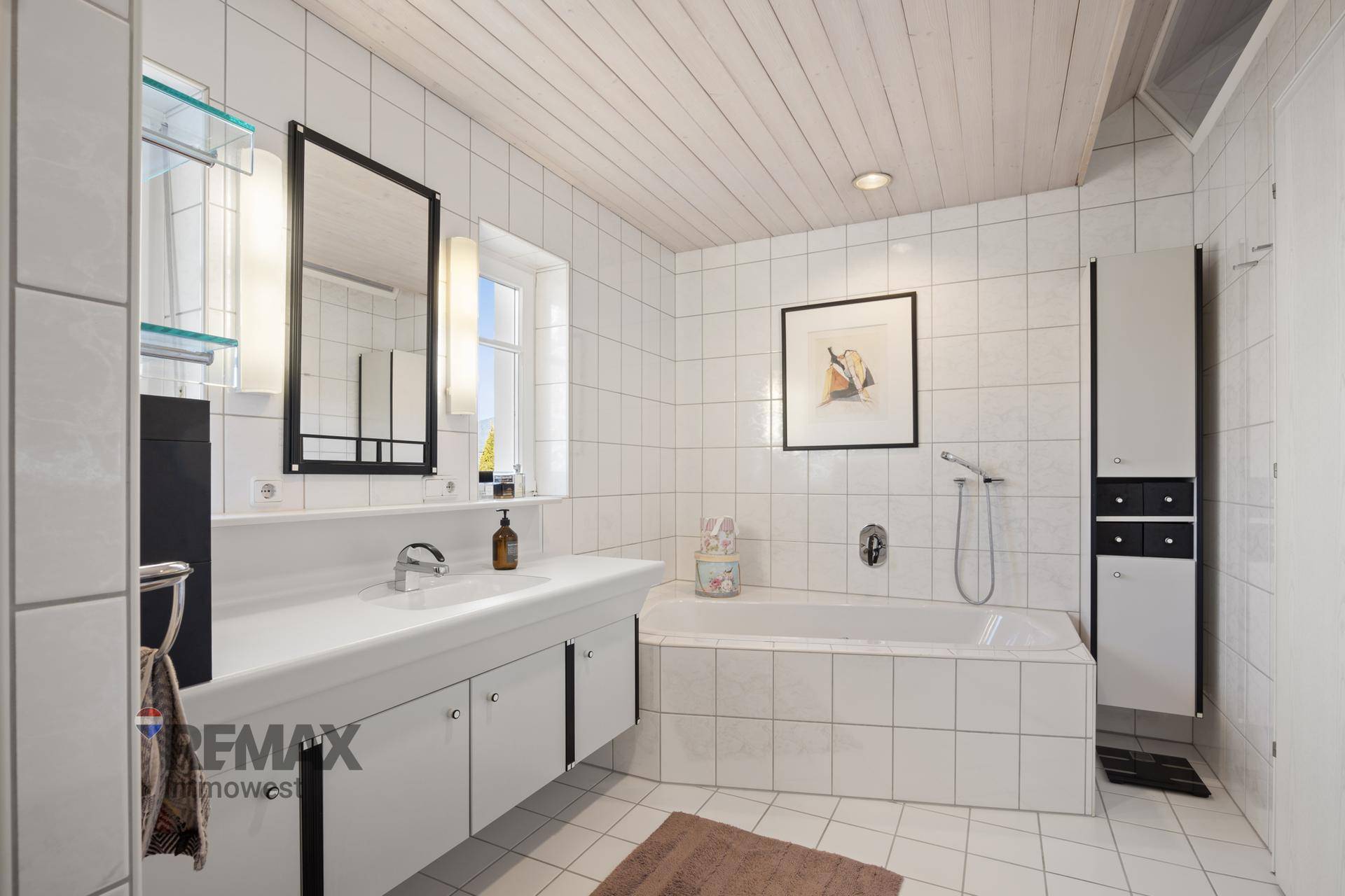Helles Badezimmer mit Badewanne, Waschbecken, Spiegel und weißen Fliesen.