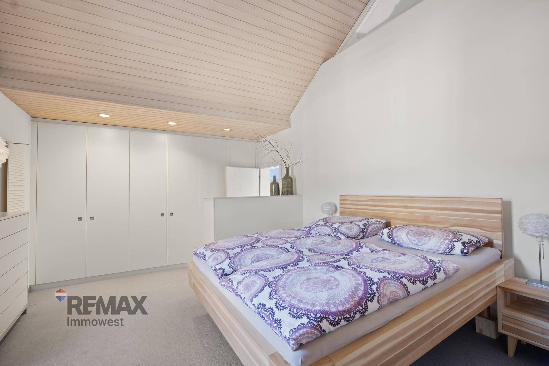 Helles Schlafzimmer mit Holzbett, Teppichboden und integrierten Kleiderschränken.