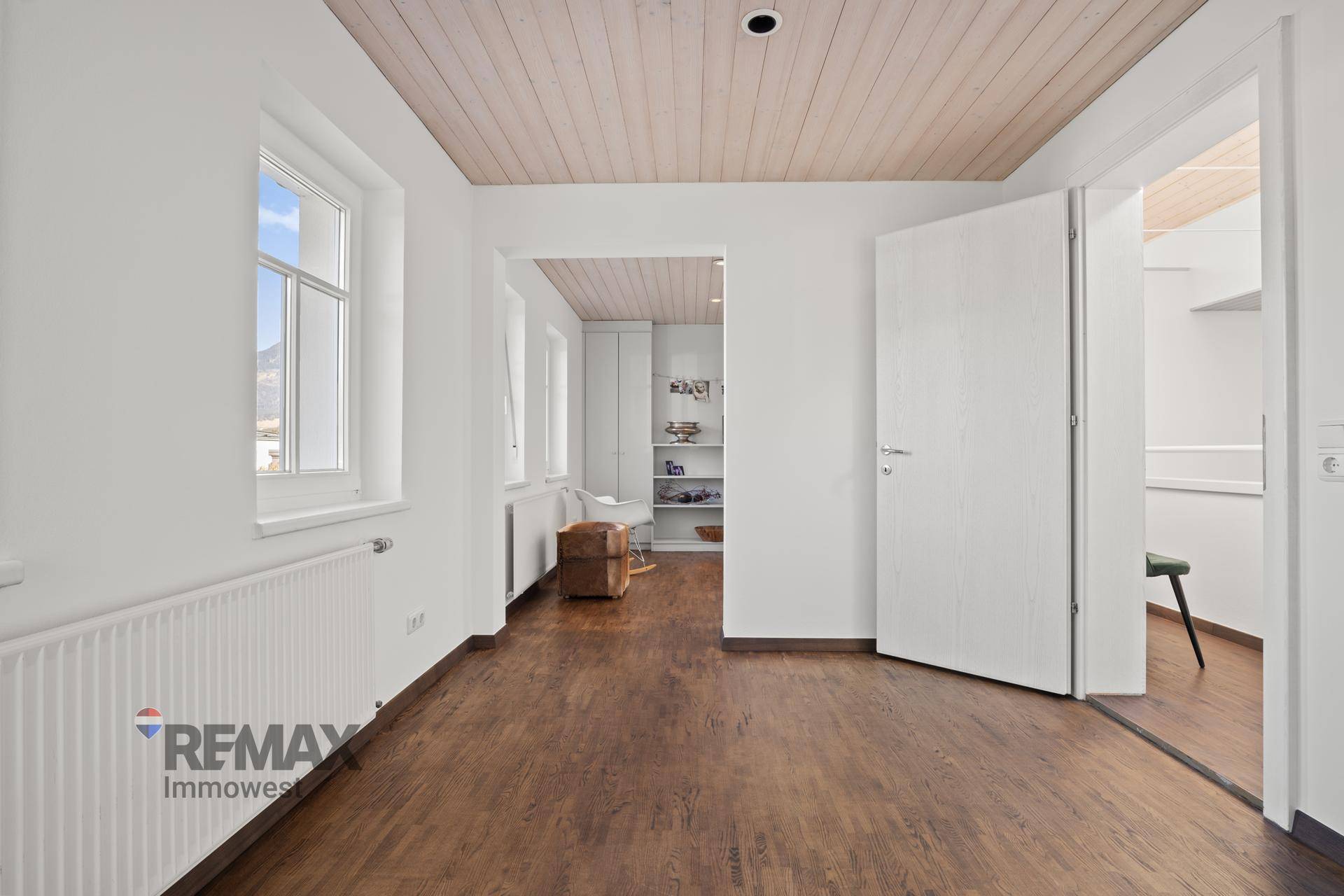 Heller, leerer Raum mit Holzboden, weißen Wänden und Blick auf die Umgebung.
