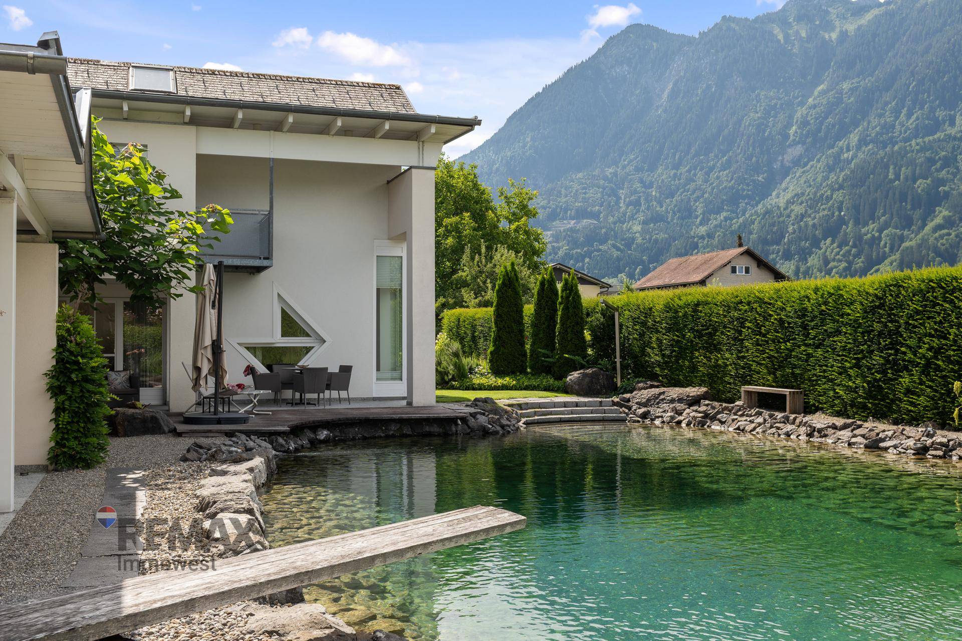 Modernes Haus mit großem Naturschwimmteich, kleiner Terrasse und beeindruckendem Bergblick.