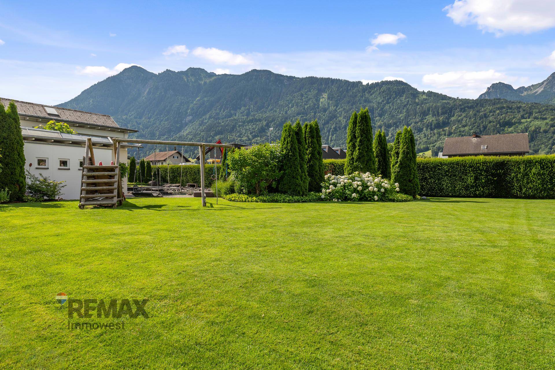 Großer Garten mit Spielplatz für Kinder, umgeben von Grünflächen und mit Blick auf die Berge.