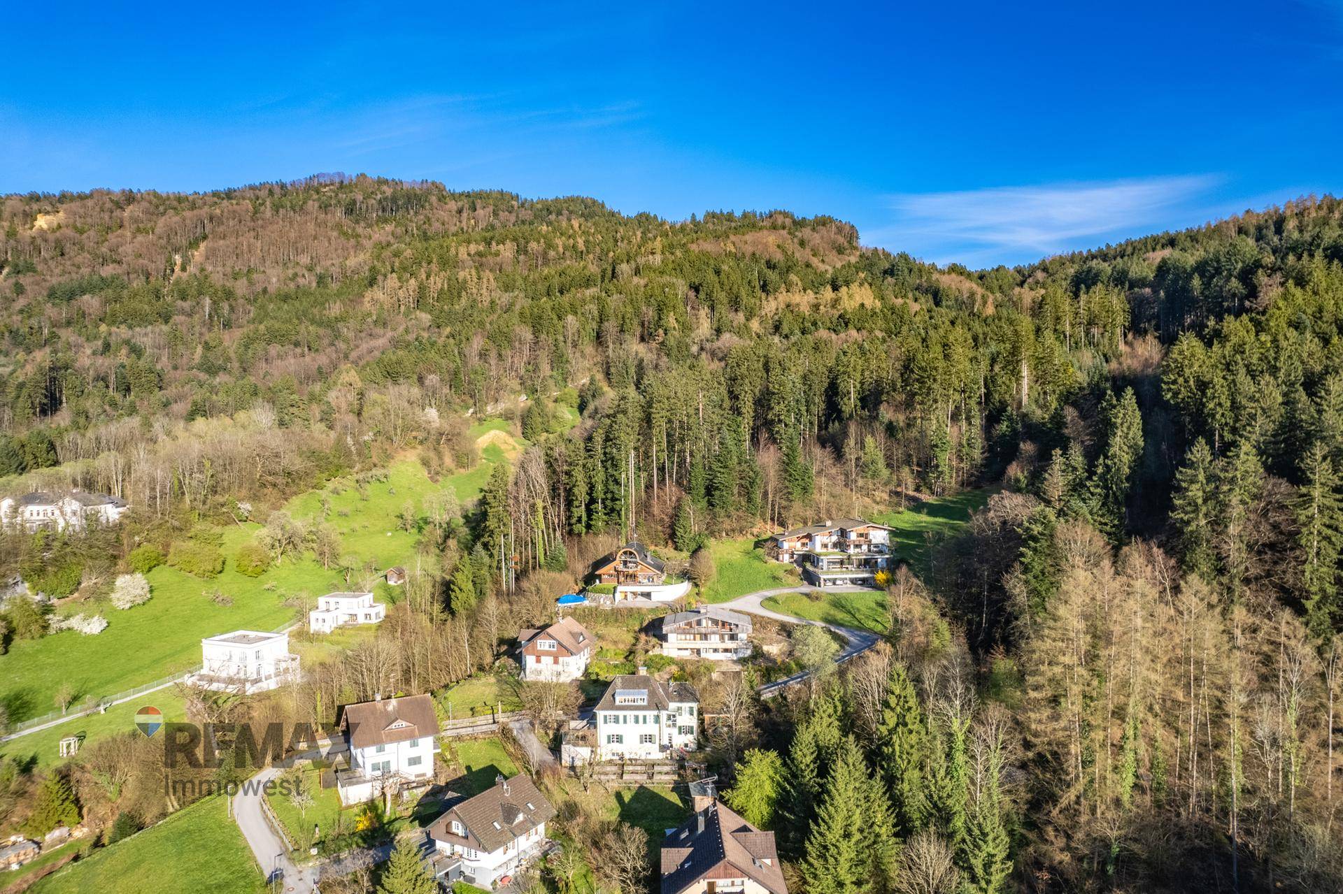 Weitläufige Luftaufnahme einer Wohnsiedlung am Hang mit dichtem Wald im Hintergrund.