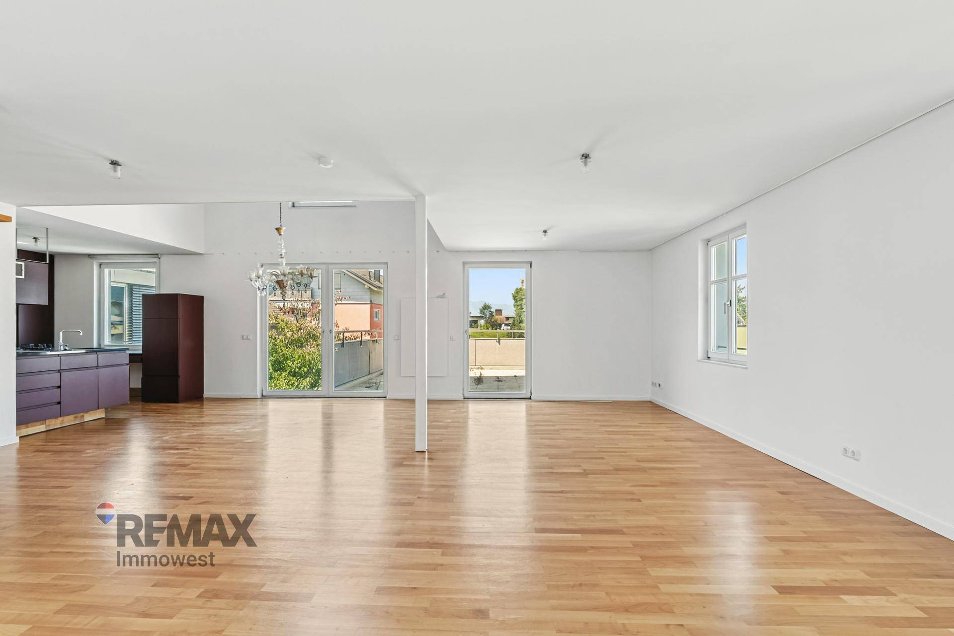 Heller, offener Wohnbereich mit Holzboden und Zugang zu einem Balkon oder einer Terrasse.