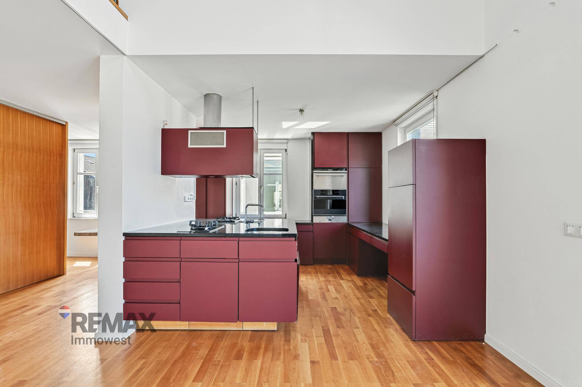 Moderne Küche in kräftigem Rot mit Kochinsel, integrierten Geräten und Holzboden.