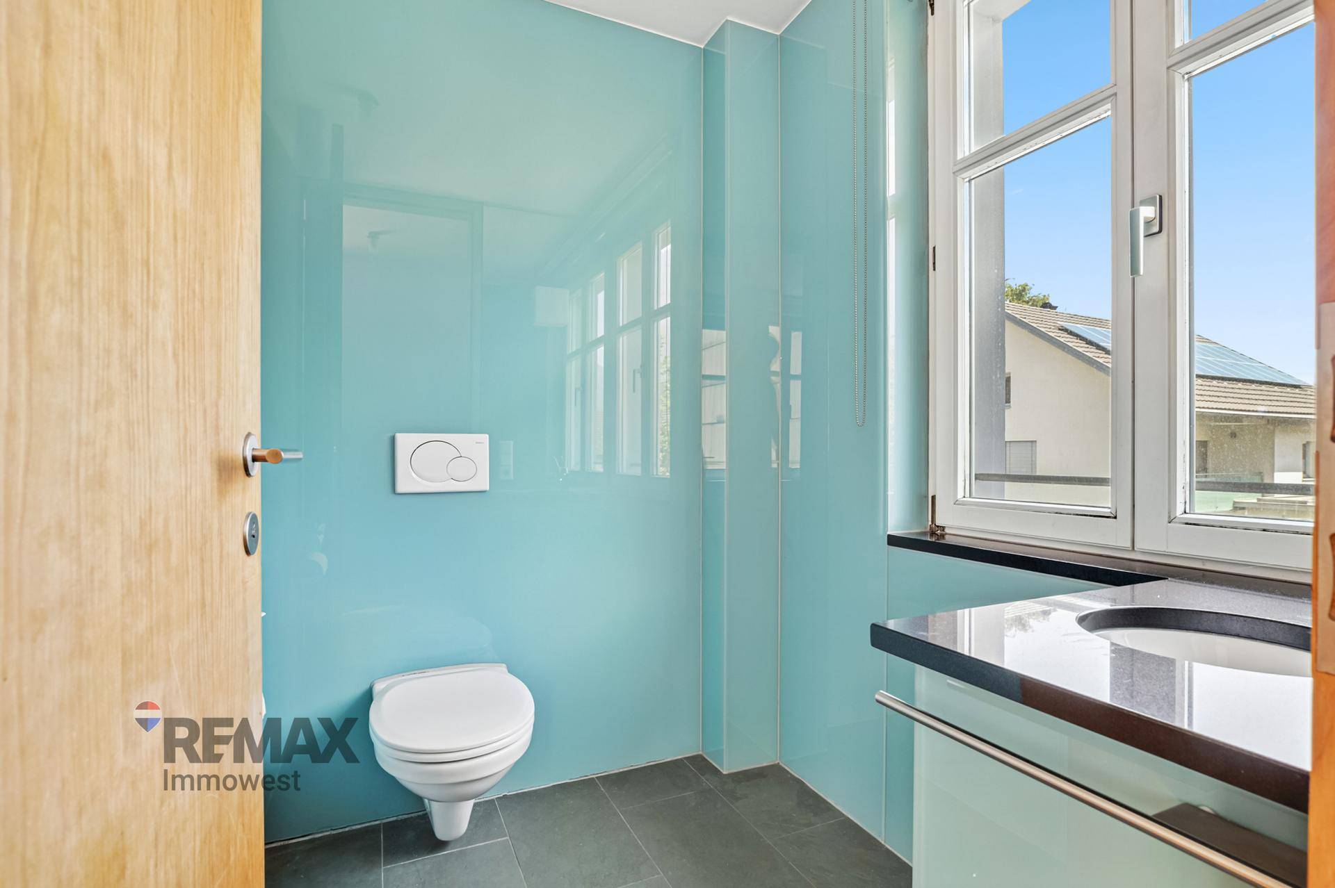Modernes Gäste-WC mit türkisfarbenen Glaswänden, Wand-WC und Fenster für Tageslicht.