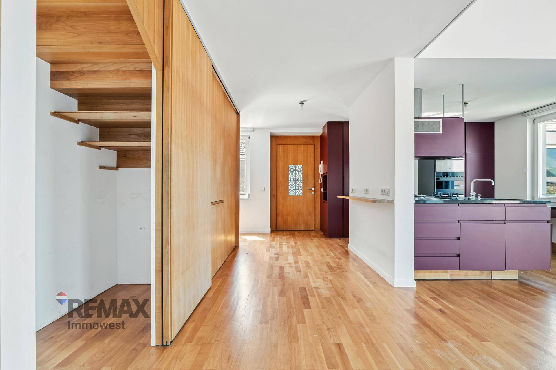 Heller Eingangsbereich mit Holzboden, integrierten Schränken und offener Treppe zur oberen Etage.