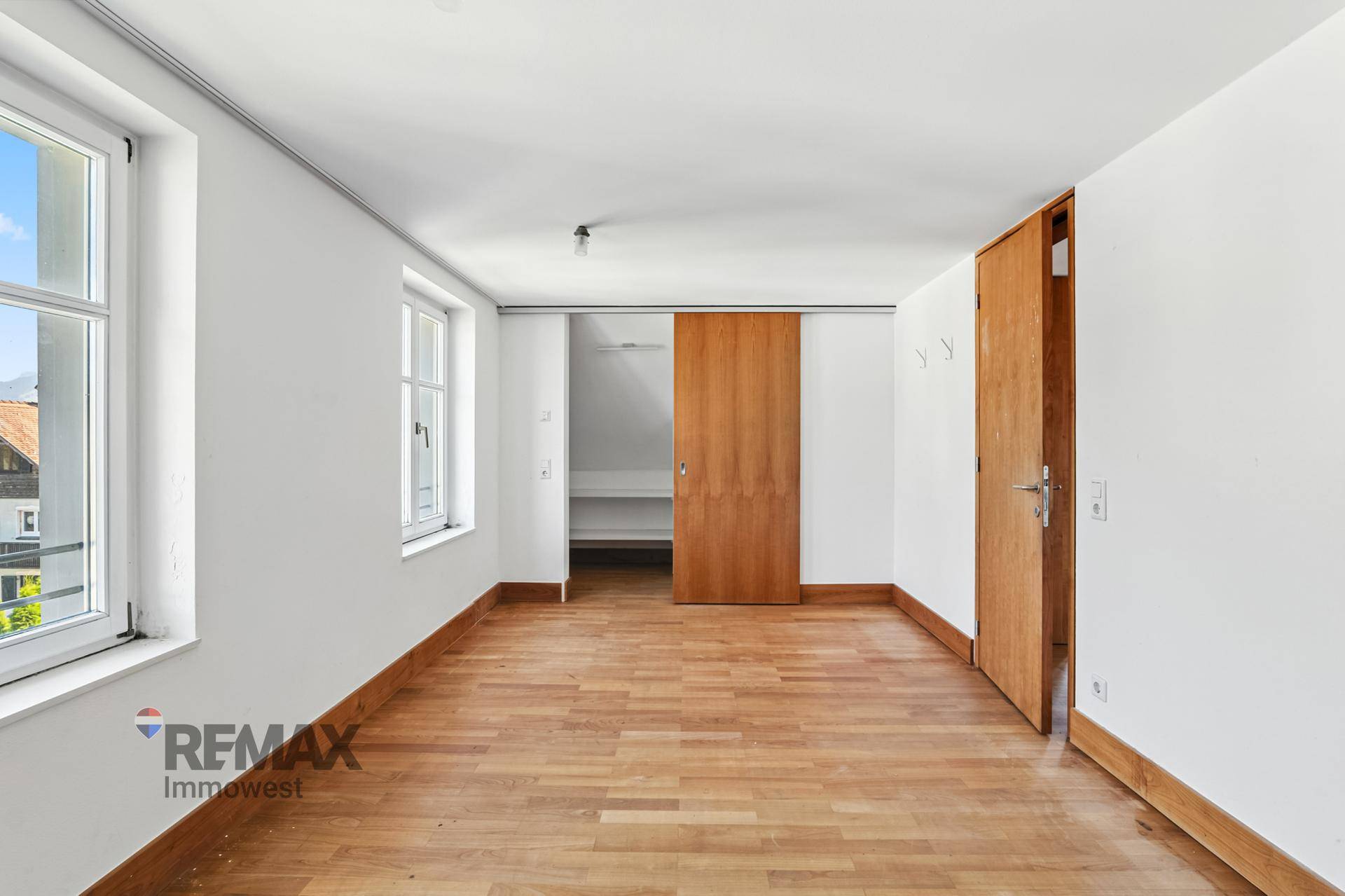 Helles Schlafzimmer mit Holzboden, großen Fenstern und Zugang zu einem Abstellraum.