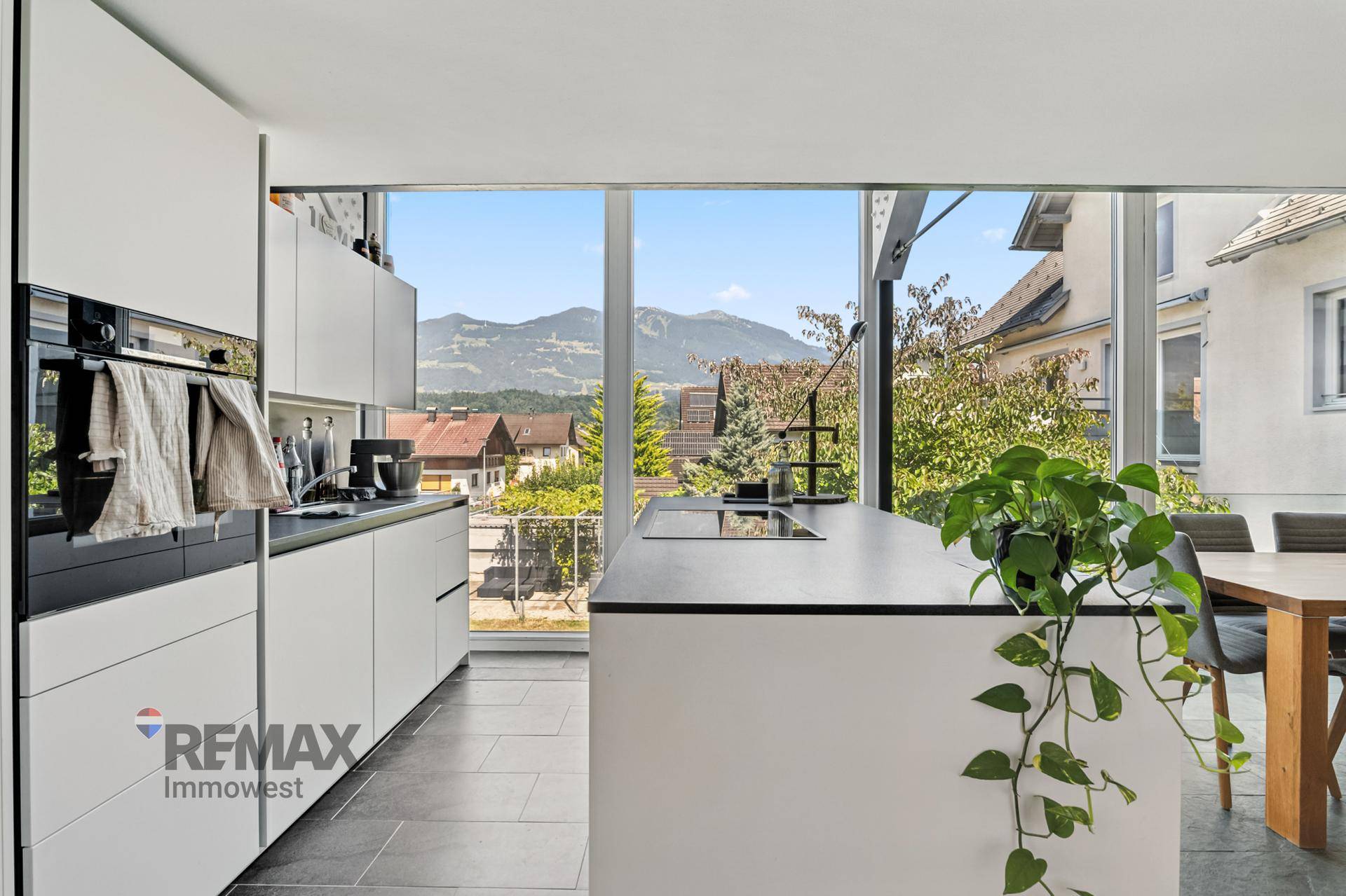Helle moderne Küche mit weißen Schränken, Kochinsel und Panoramafenstern mit Bergblick.