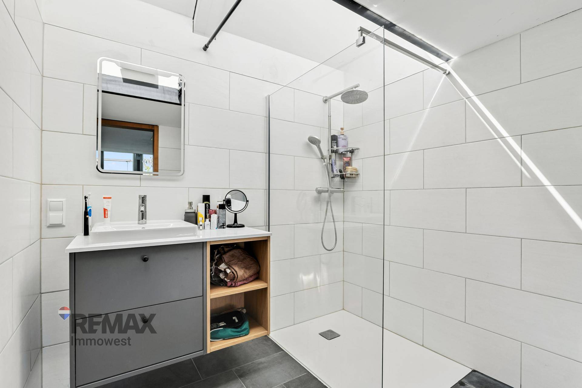 Modernes Badezimmer mit großer begehbarer Dusche, Einzelwaschbecken und weißen Fliesen.