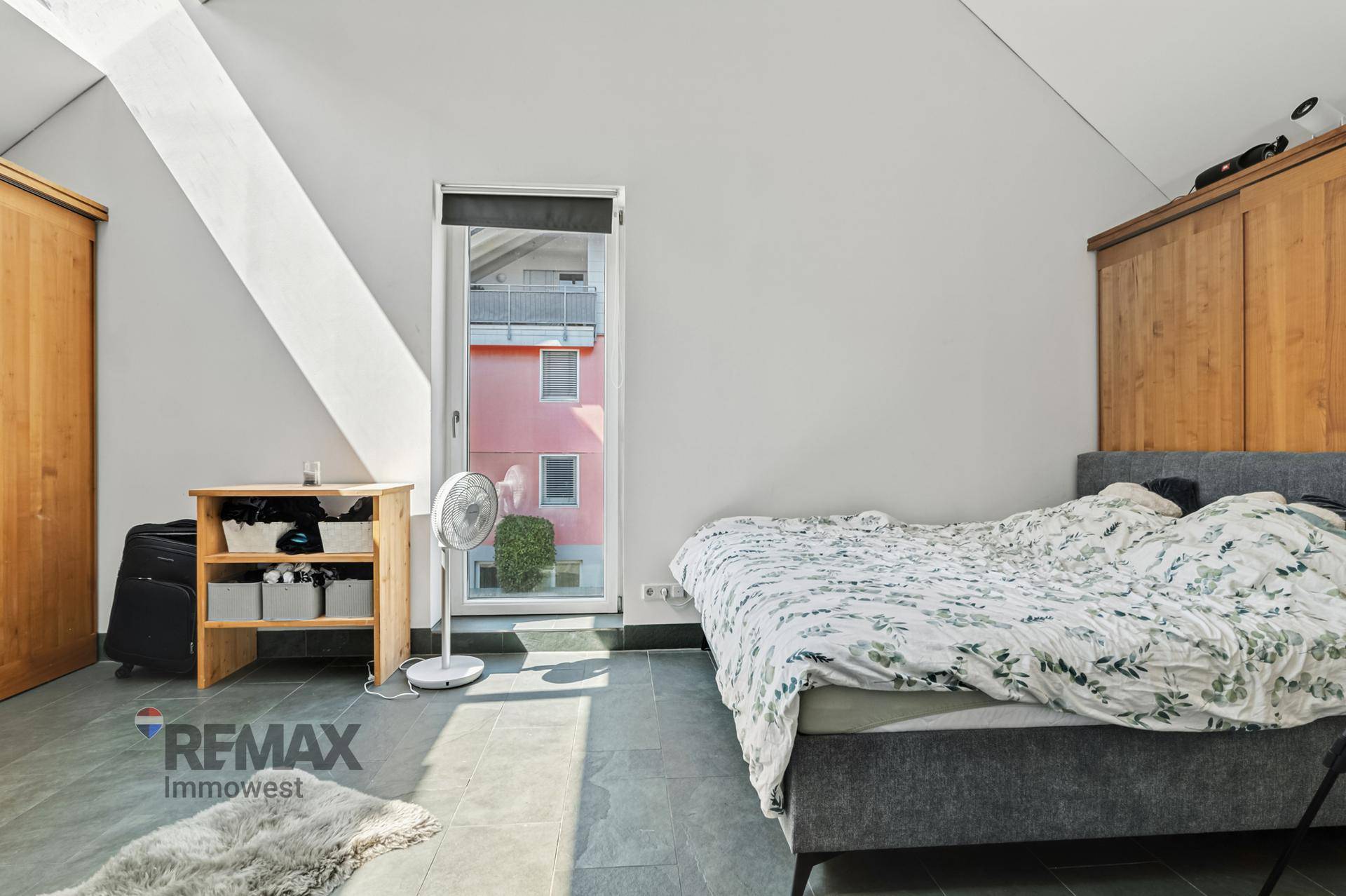 Helles Schlafzimmer mit Bett, Fliesenboden und Zugang zu einem französischen Balkon.