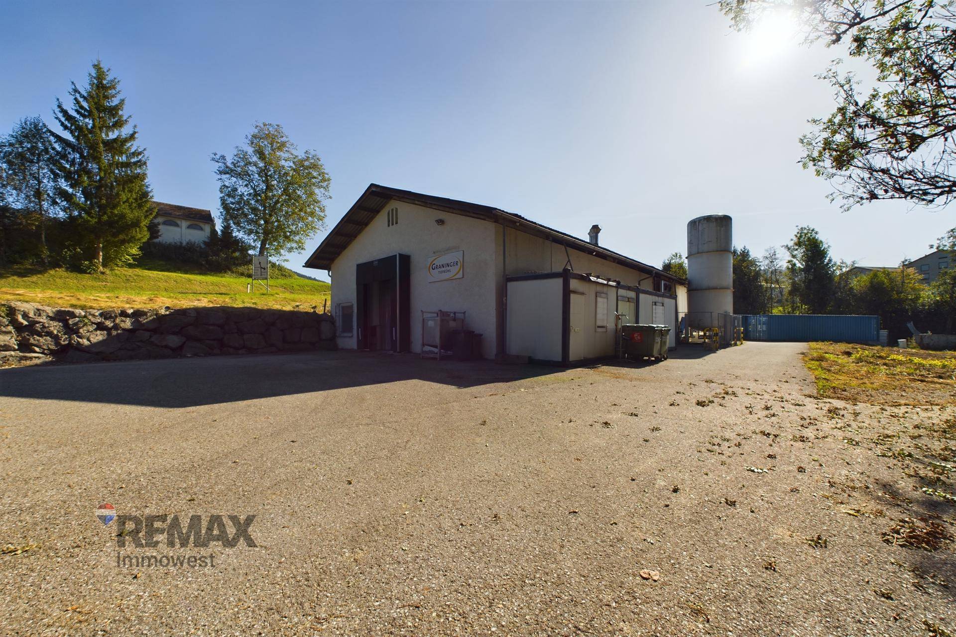 Außenansicht eines Gewerbegebäudes mit großem Vorplatz und grüner Umgebung unter strahlendem Sonnenschein.