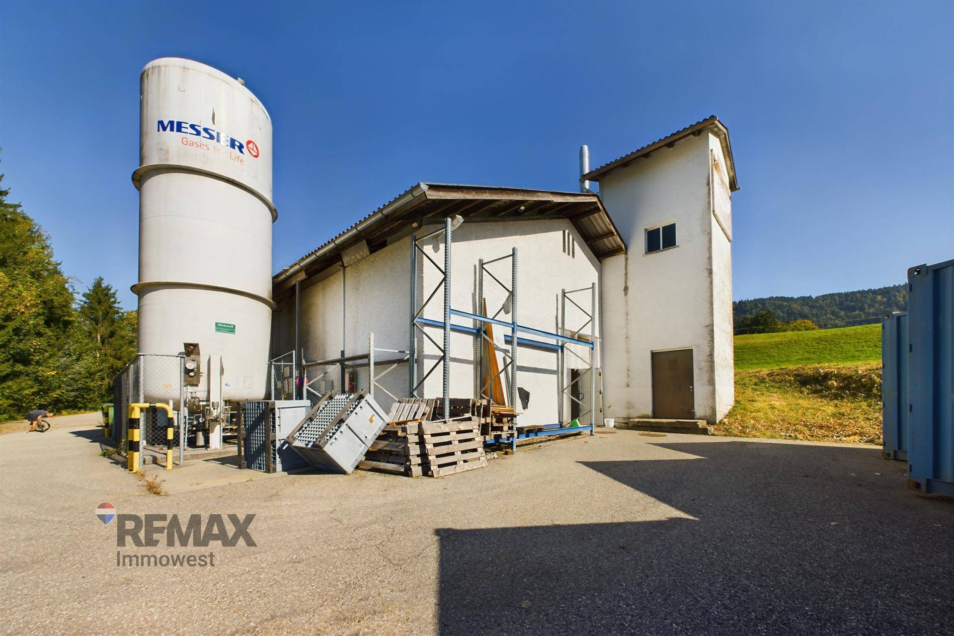Rückansicht des Gewerbegebäudes mit großem weißen Silo und Außenlagerflächen in ländlicher Umgebung.