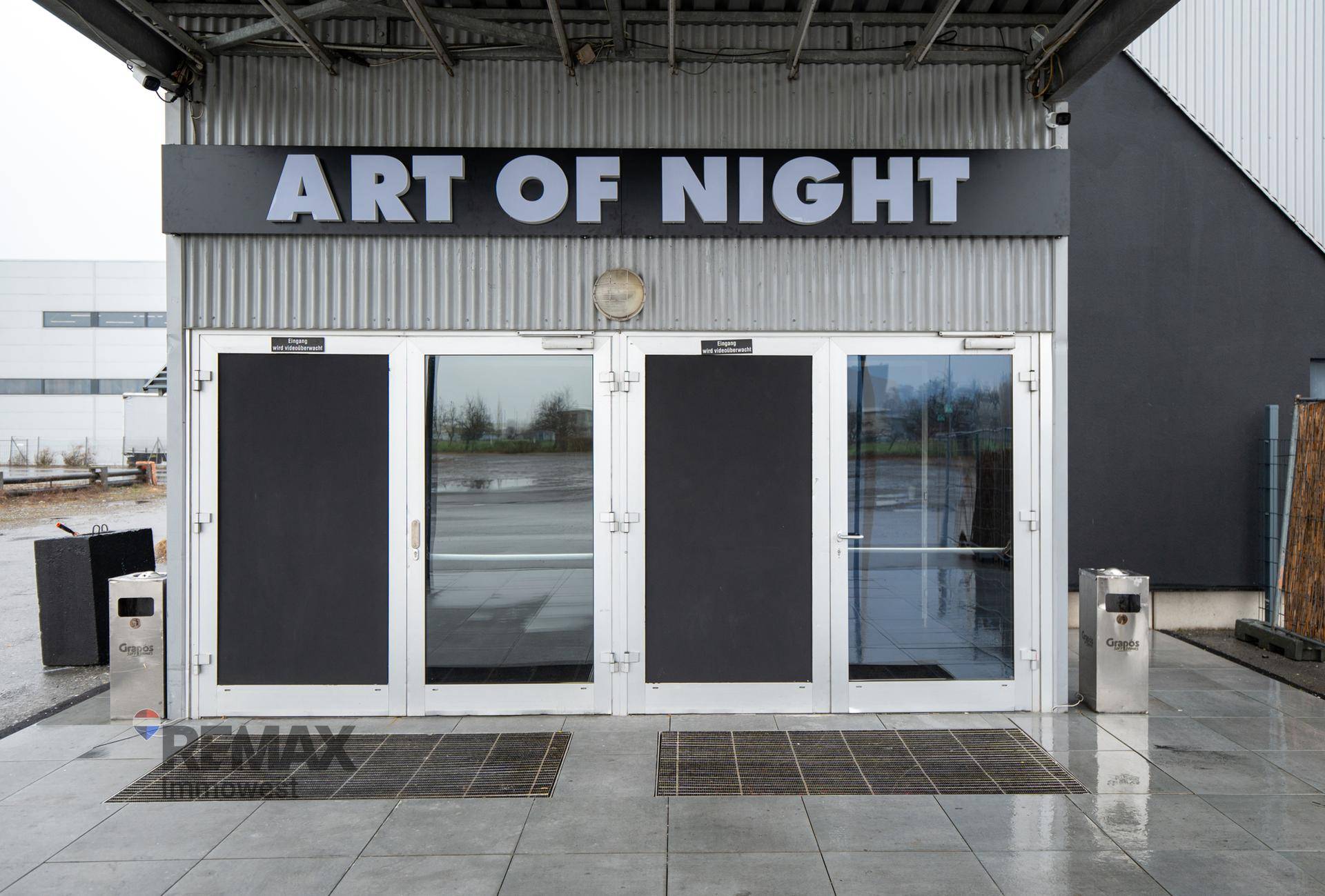 Eingangsbereich des Gebäudes mit großen Glastüren und markanter Beschilderung "ART OF NIGHT".