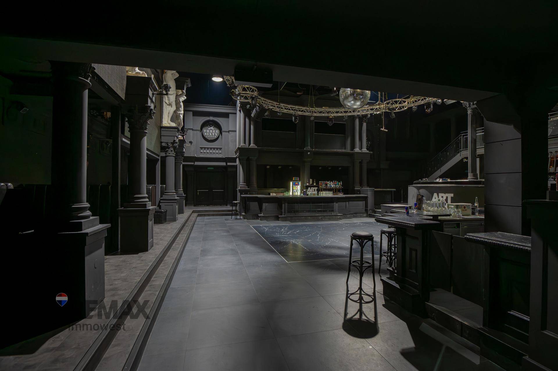 Großer, dunkler Tanzsaal mit Säulen, einer Bar und einer Discokugel, bereit für Veranstaltungen.