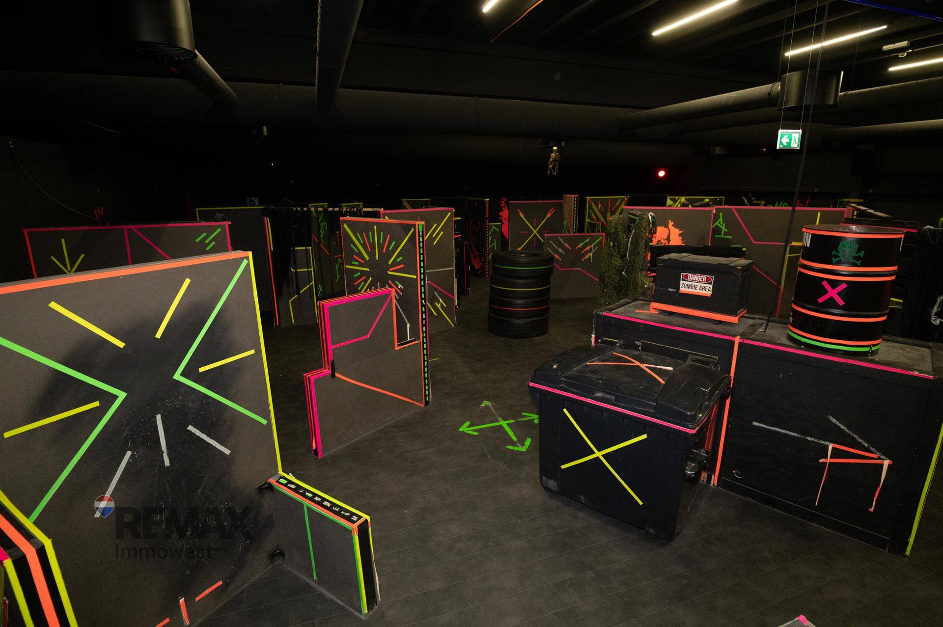 Dunkle Laser-Tag-Arena mit leuchtenden Hindernissen und Neonfarben für spannende Spiele.
