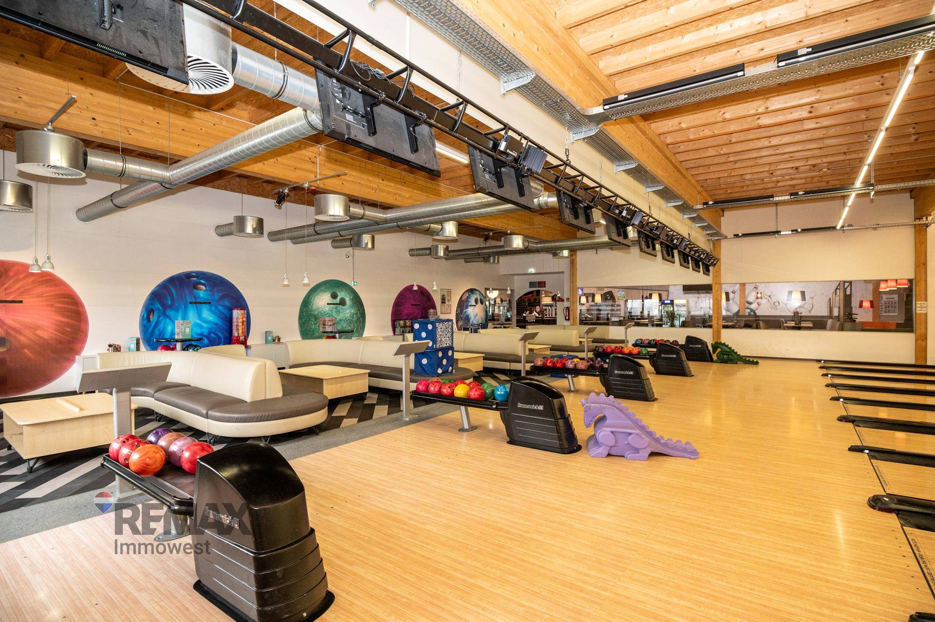 Weitläufige Bowlinghalle mit mehreren Bahnen, Sitzgelegenheiten und Holzbalkendecke.