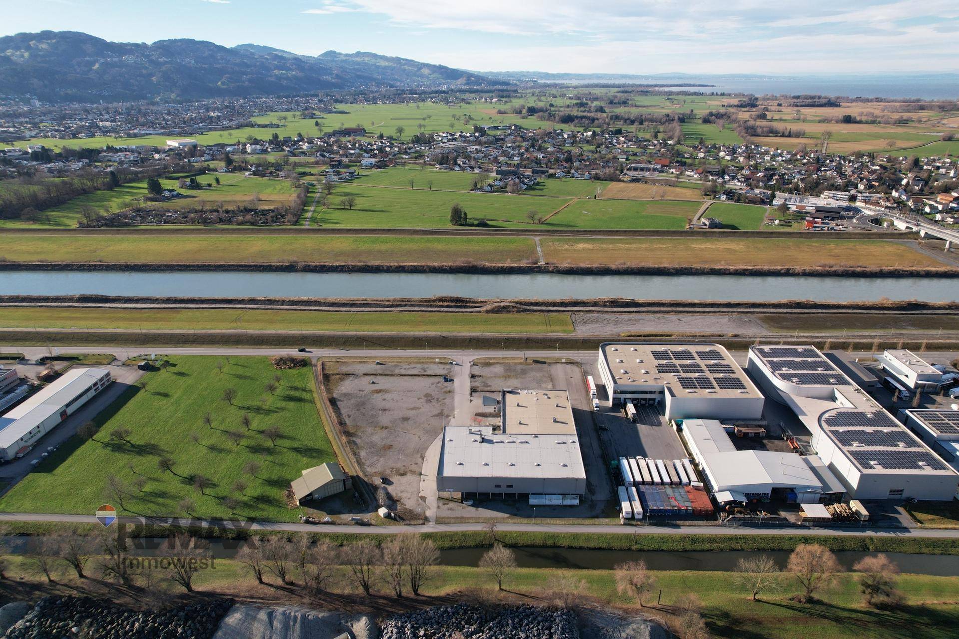 Luftaufnahme des Gewerbegebiets mit grünen Feldern, Kanälen und Bergen im Hintergrund, idyllische Lage.