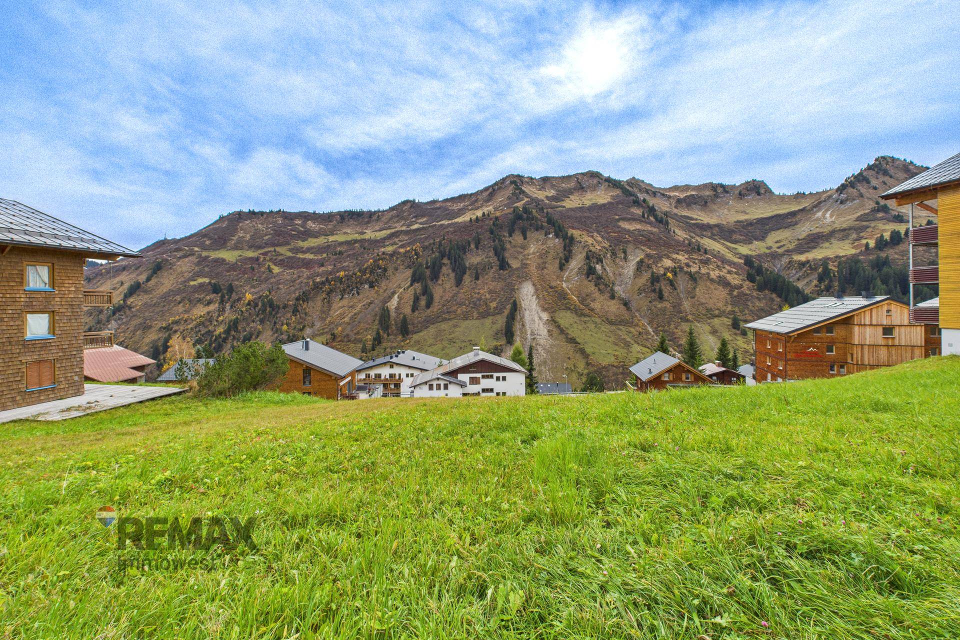 Grüne Wiese mit Blick auf eine Ansammlung von Häusern und majestätische Berge im Hintergrund.