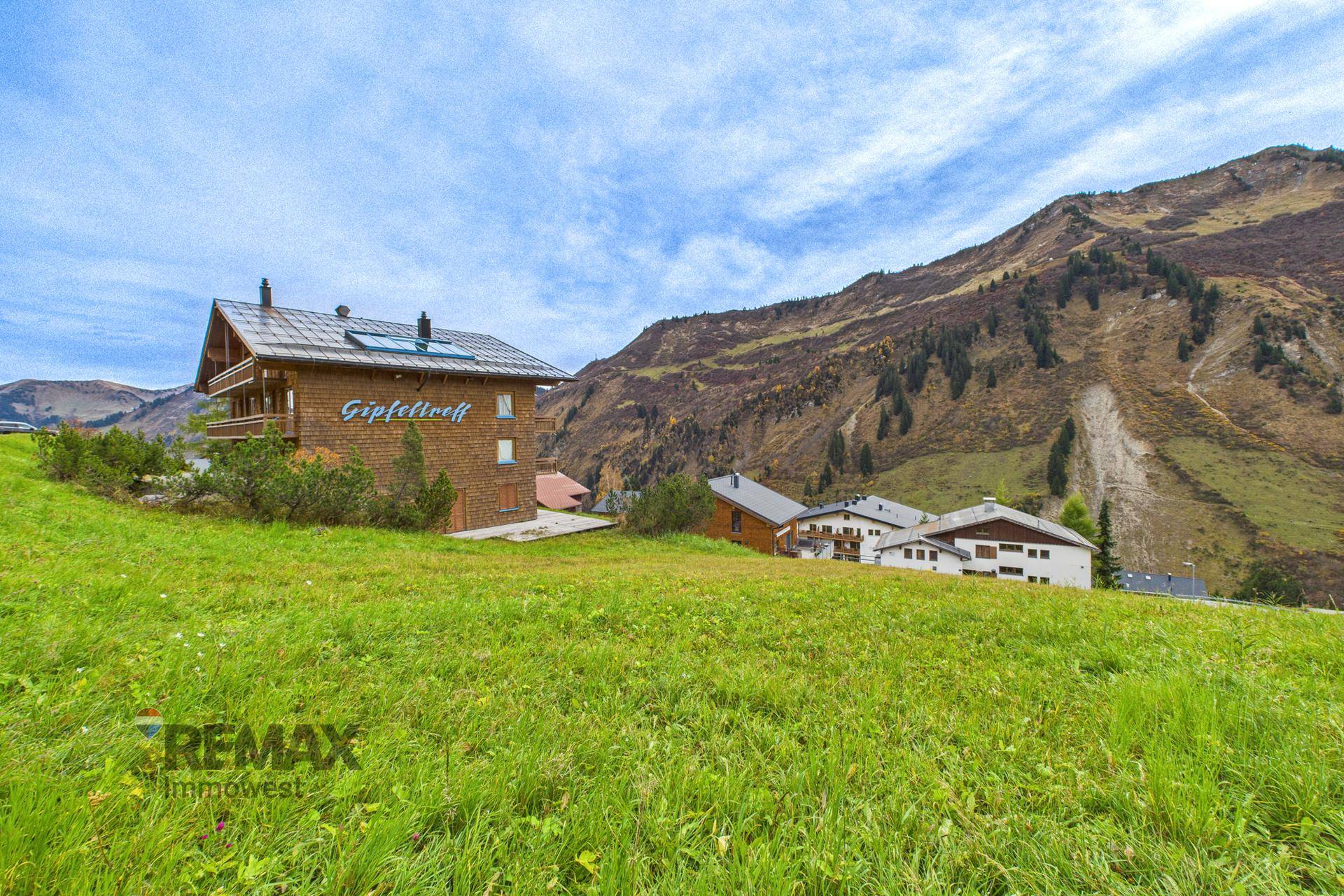Traditionelles Holzchalet mit Bergblick, umgeben von grünen Wiesen und alpiner Landschaft.