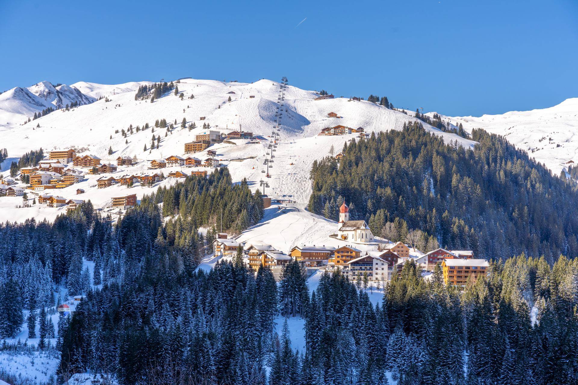 Malerisches Bergdorf im Winter mit verschneiten Dächern, Skipisten und Liftanlagen.