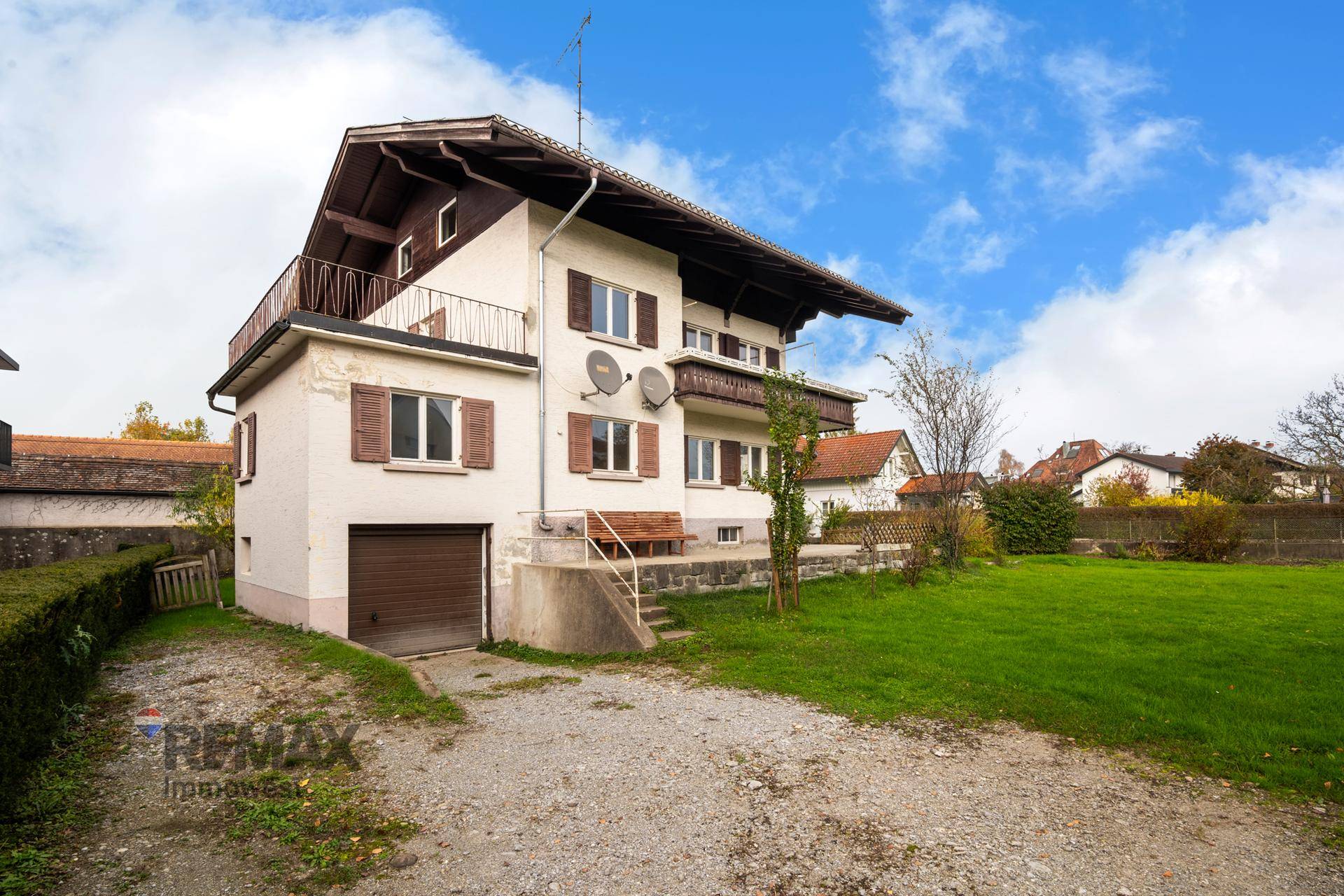 Rückansicht des Hauses mit integrierter Garage, großem Gartenbereich und Balkon im Obergeschoss.