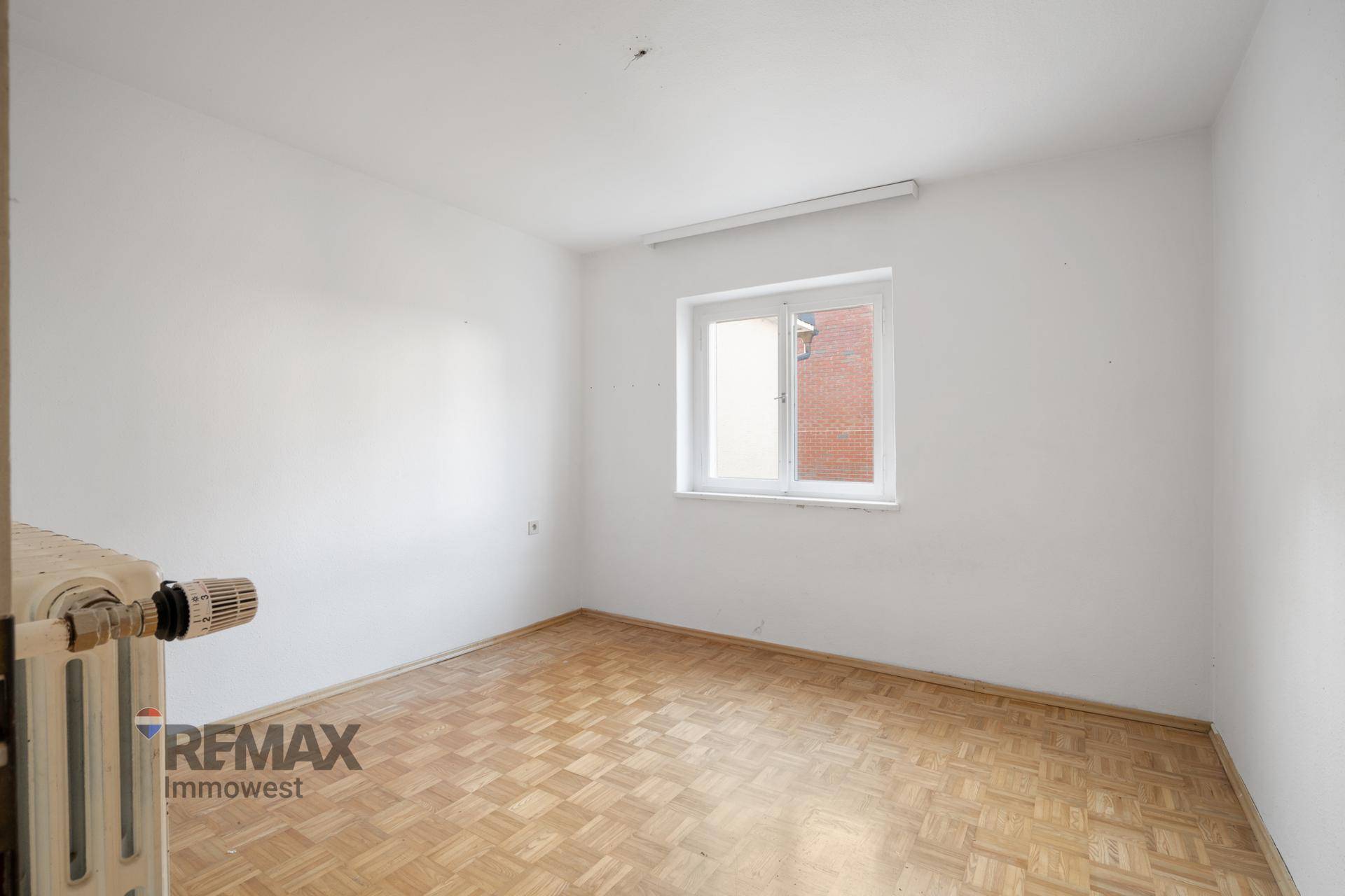 Helles Zimmer mit Parkettboden und einem Fenster, das viel Tageslicht hereinlässt.