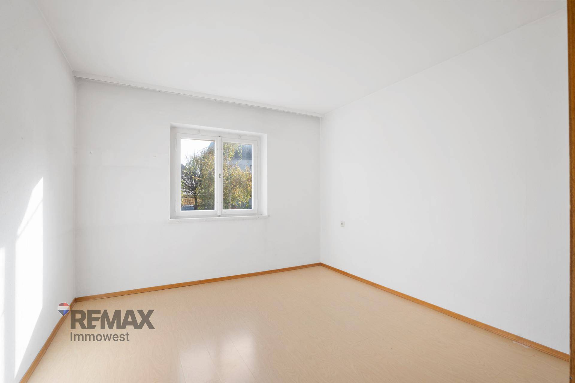 Einfaches Zimmer mit hellem Bodenbelag und einem Fenster, das den Raum erhellt.