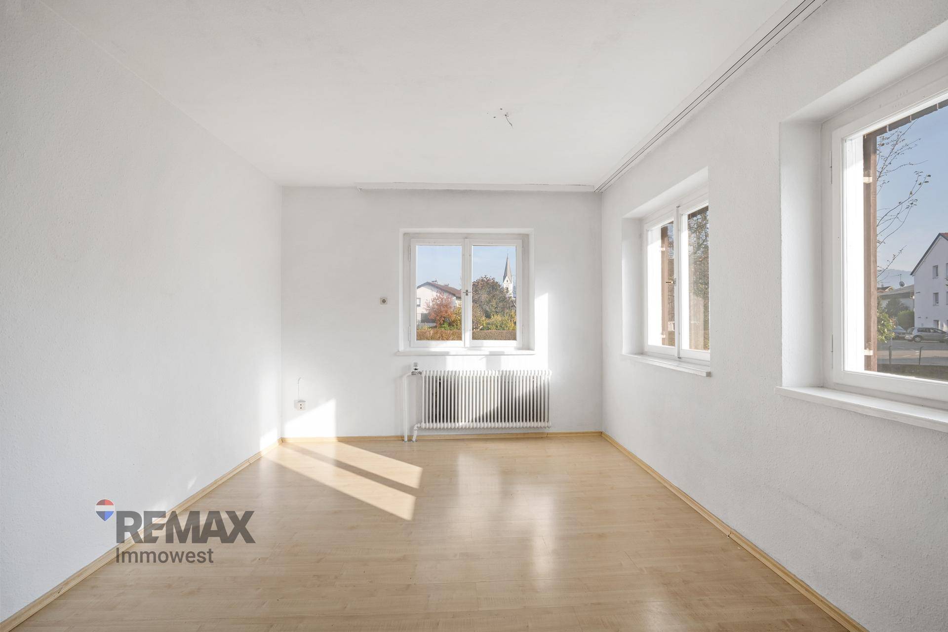 Geräumiges Wohnzimmer mit hellem Laminatboden und großen Fenstern für viel Tageslicht.