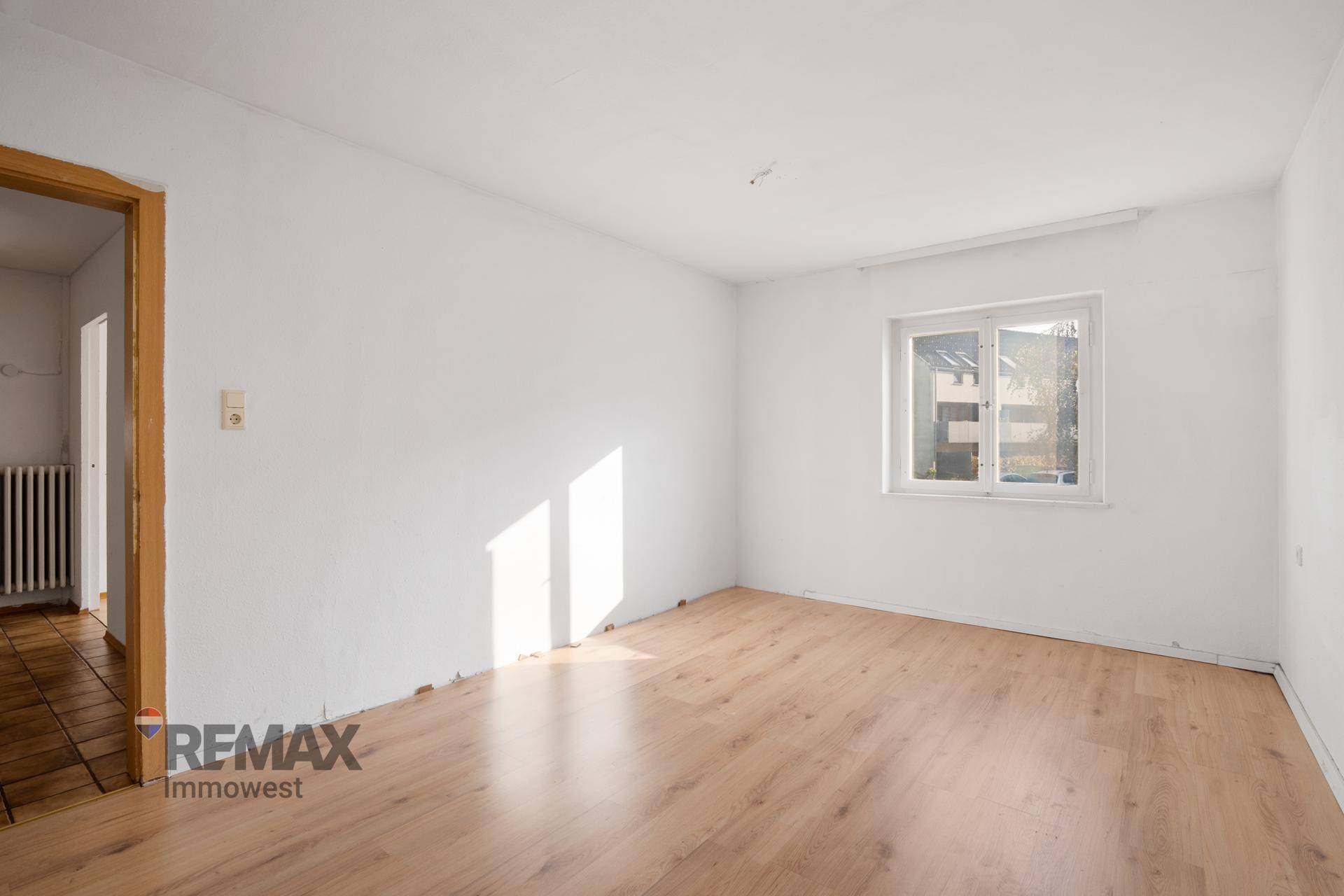 Helles Zimmer mit Laminatboden und einem Fenster, das den Raum mit Sonnenlicht durchflutet.