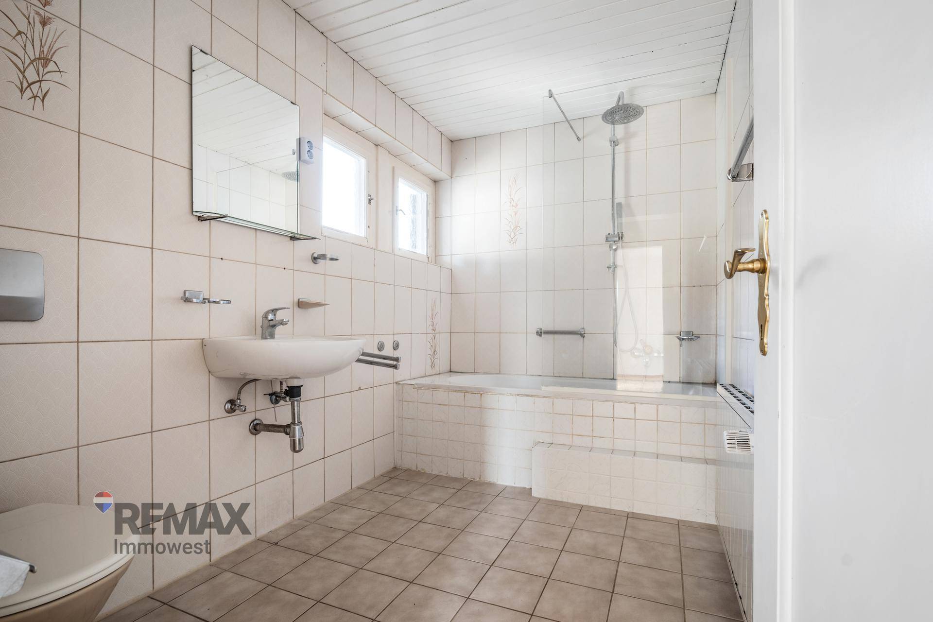 Gefliestes Badezimmer mit Badewanne, Dusche und Fenster für natürliche Belüftung.
