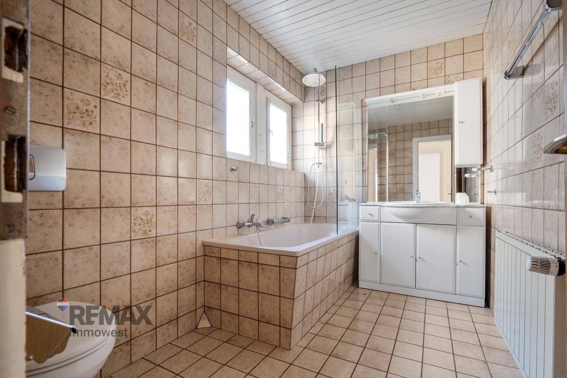 Gefliestes Badezimmer mit Badewanne, Waschtisch und Fenster für Tageslicht.
